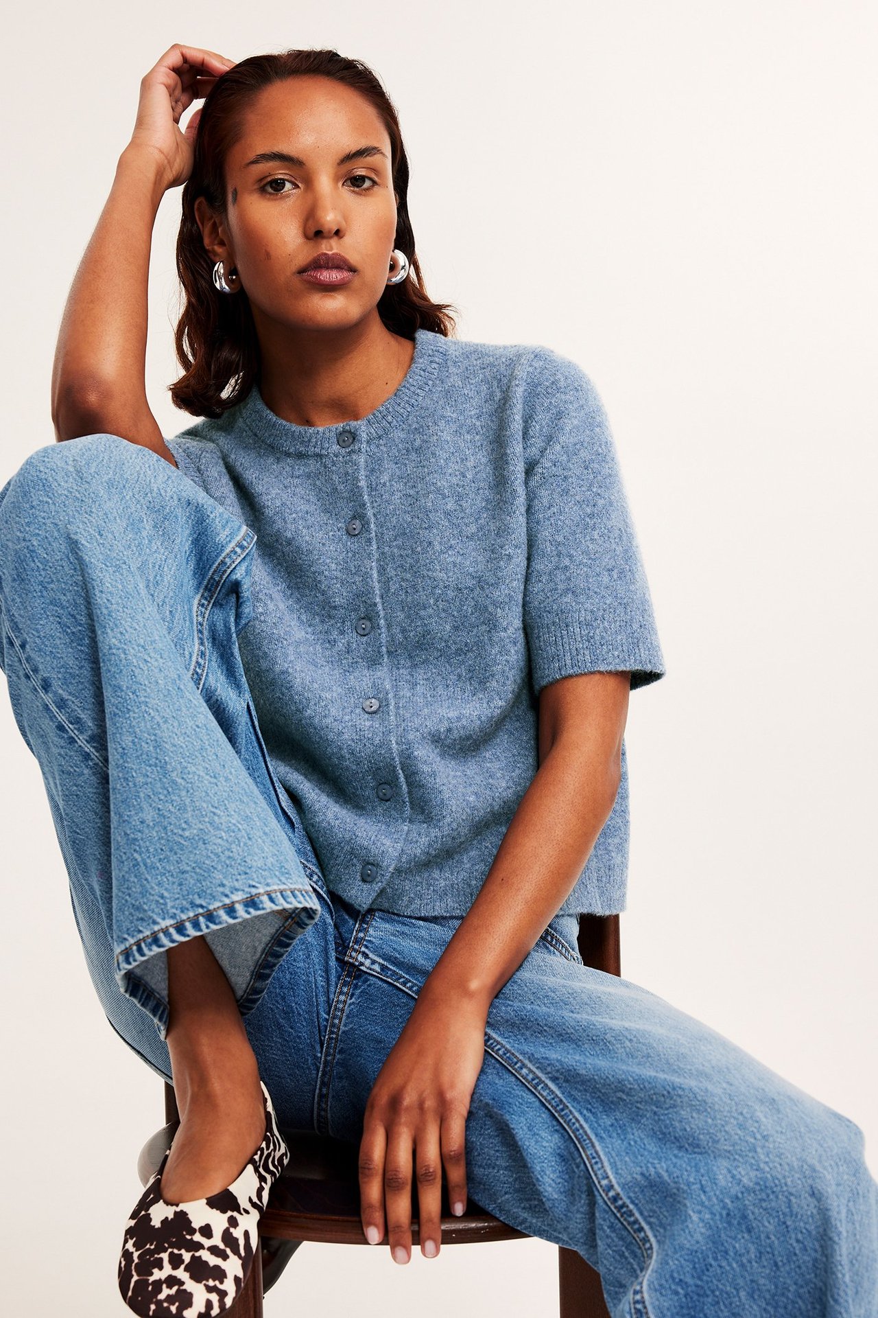 Vaaleansininen meleerattu lyhythihainen neuletakki, siniset farkut ja lehmäkuvioiset ballerinat.