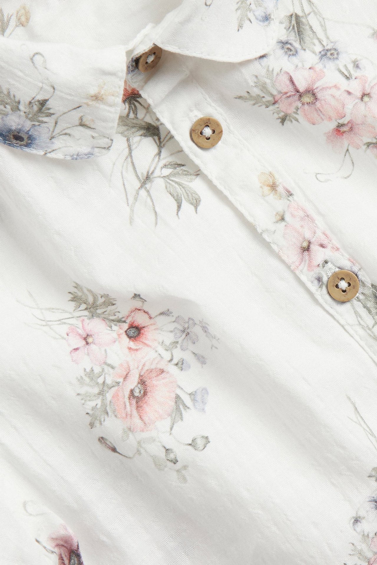 Zbliżenie na ecru bawełnianą koszulę z krótkim rękawem, kwiatowym wzorem i drewnianymi guzikami.