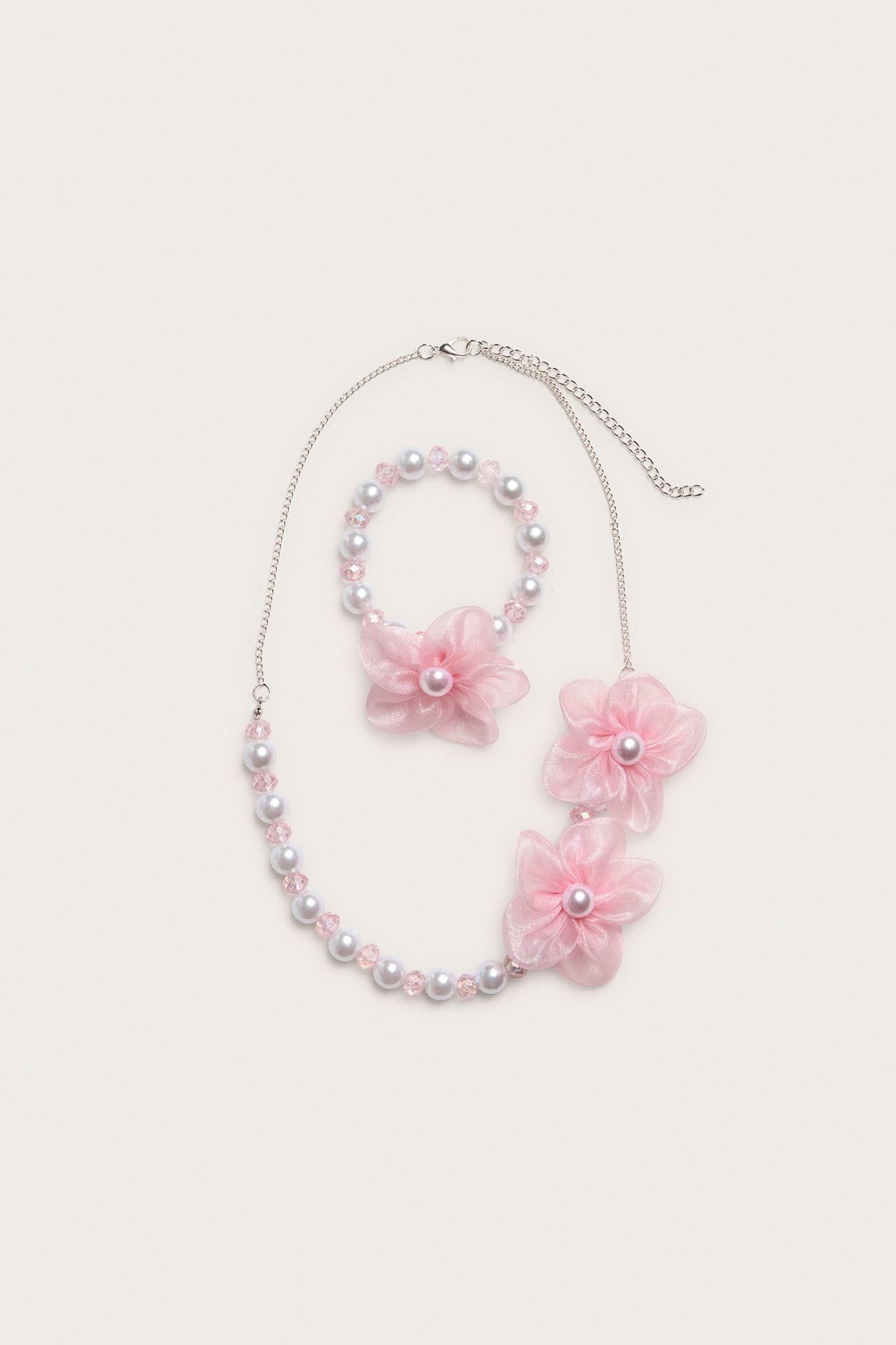 Ovenfra: Lys rosa og hvitt perlekjede med tre gjennomsiktige rosa blomsterdetaljer, matchende armbånd.