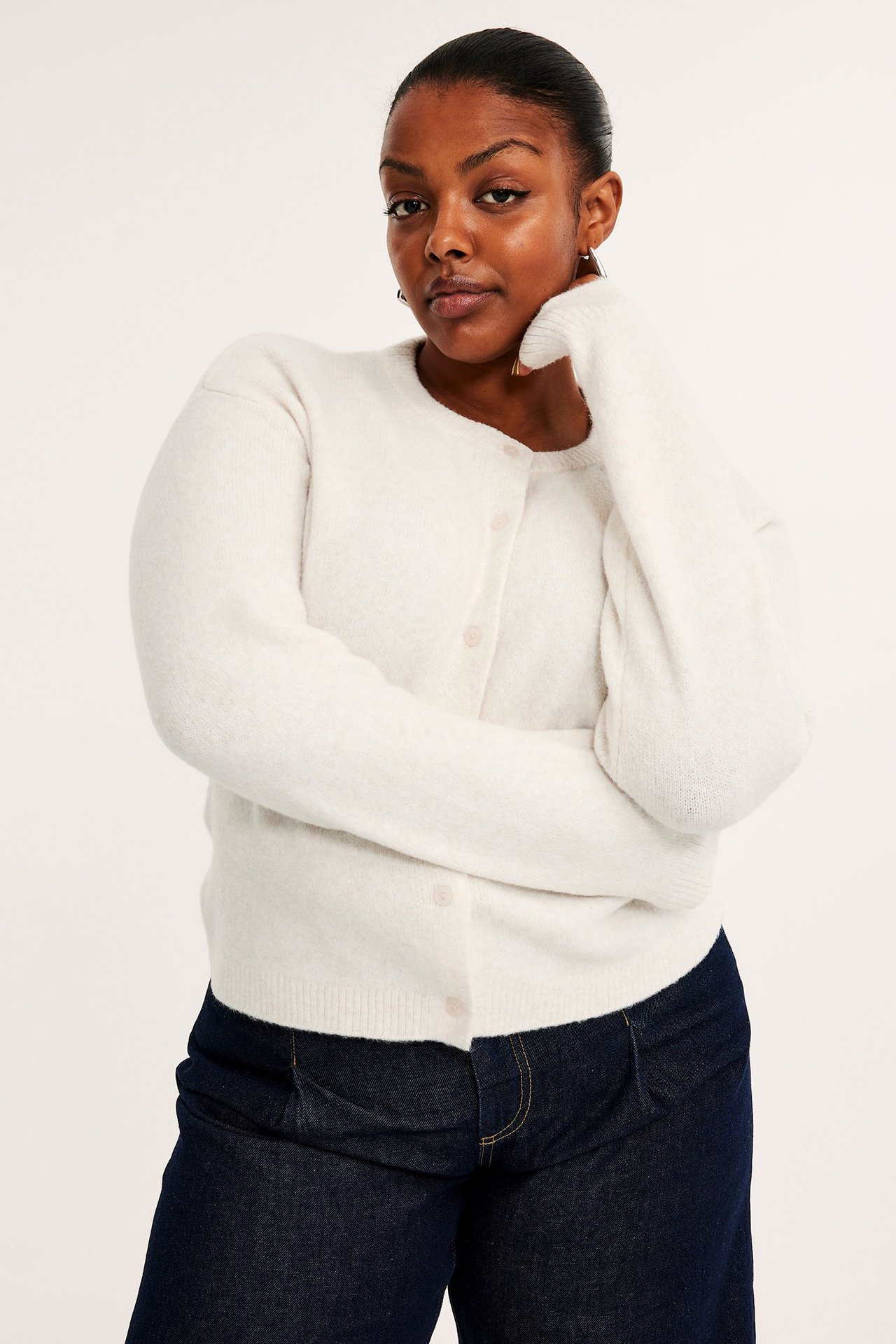 Forfra: Kvinne i lys beige finstrikket cardigan med knapper og mørkeblå jeans.