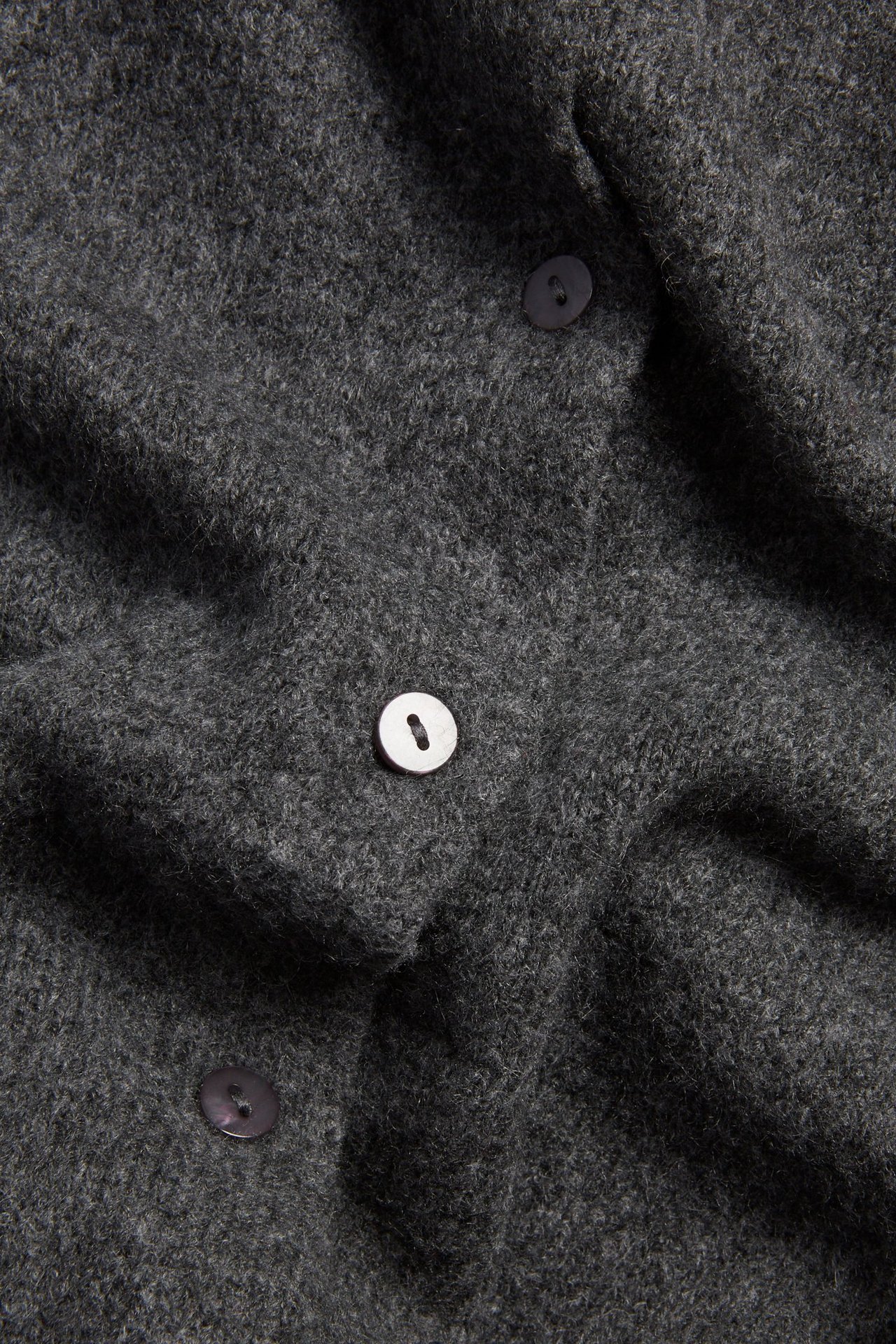 Zbliżenie na ciemnoszary, drobno dziergany kardigan z trzema guzikami, jednym jasnym i dwoma ciemnymi.