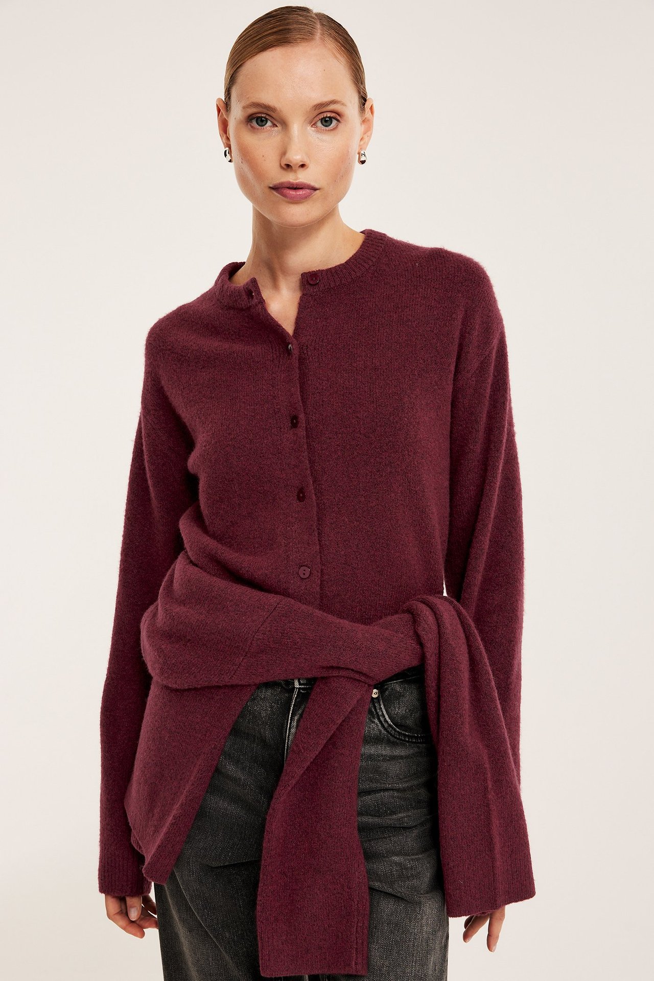 Etuvaaka, nainen tummanpunaisessa hienoneulotussa neuletakissa, toinen sidottuna vyötärölle.