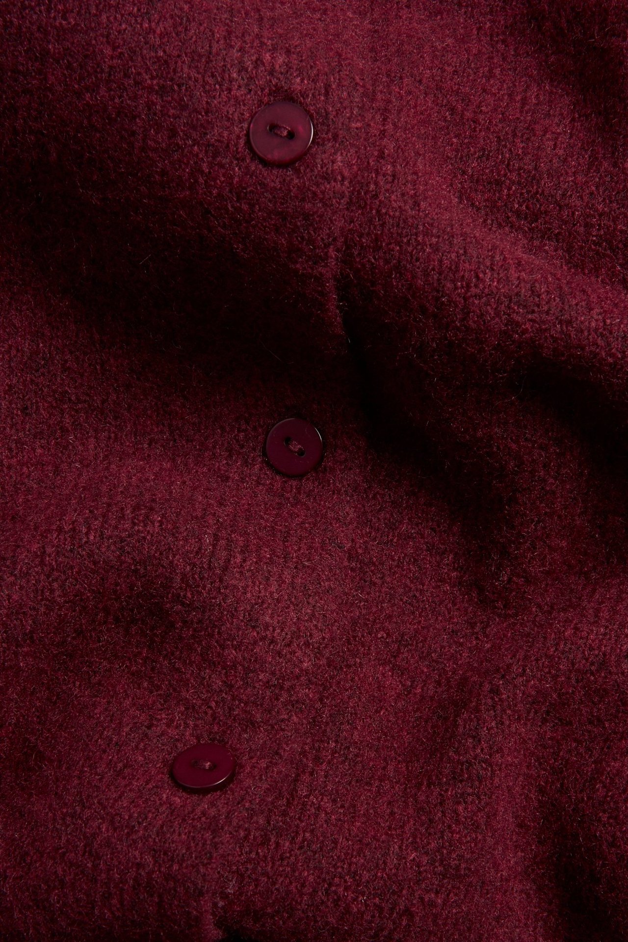 Zbliżenie na ciemnoczerwony, drobno tkany kardigan z trzema pasującymi guzikami.