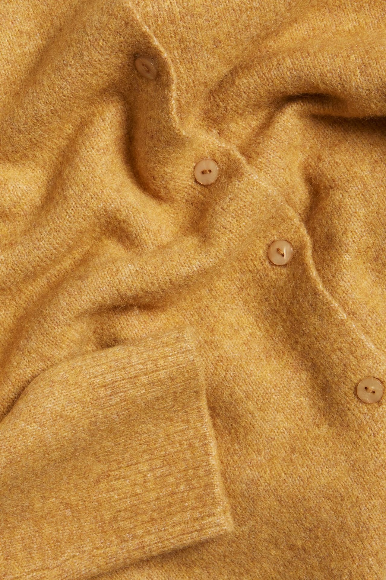 Zbliżenie żółtego, drobno dzianego kardiganu z jasnobrązowymi guzikami.