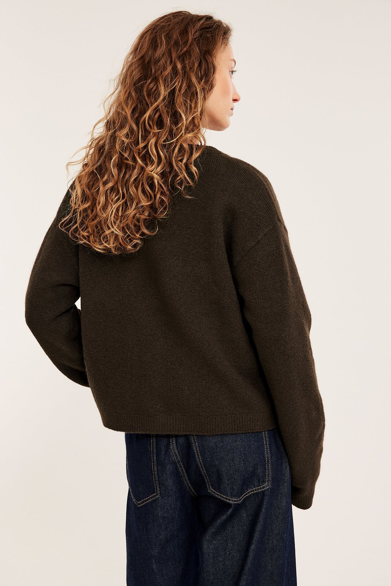 Ryggvy av en kvinna i en mörkbrun enfärgad finstickad kofta över mörkblå lösa jeans.