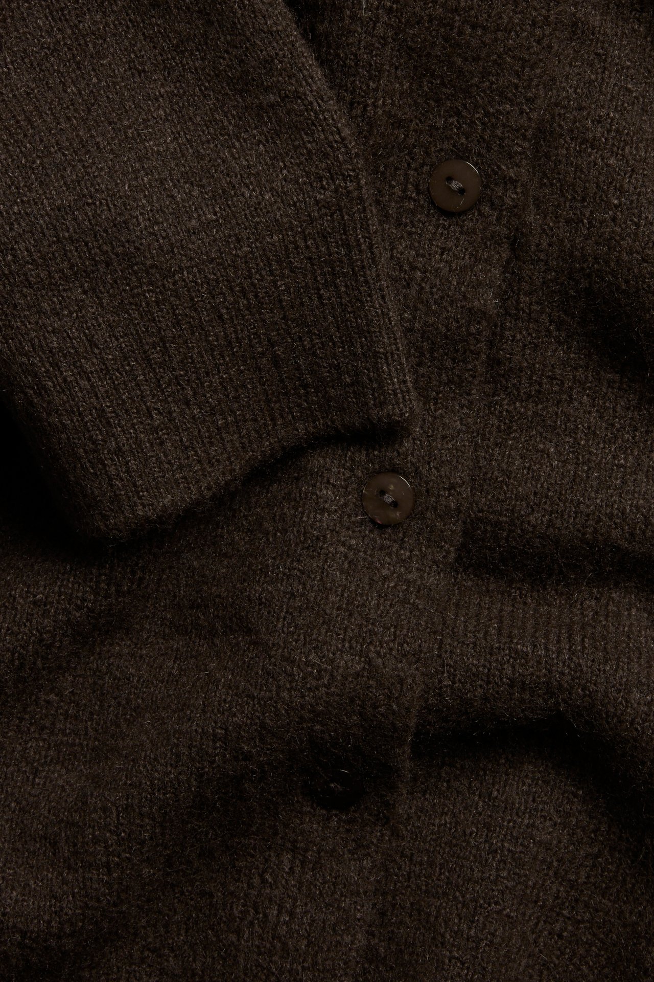 Nærbilde av en mørkebrun finstrikket cardigan med synlige knapper og ribbet mansjett.