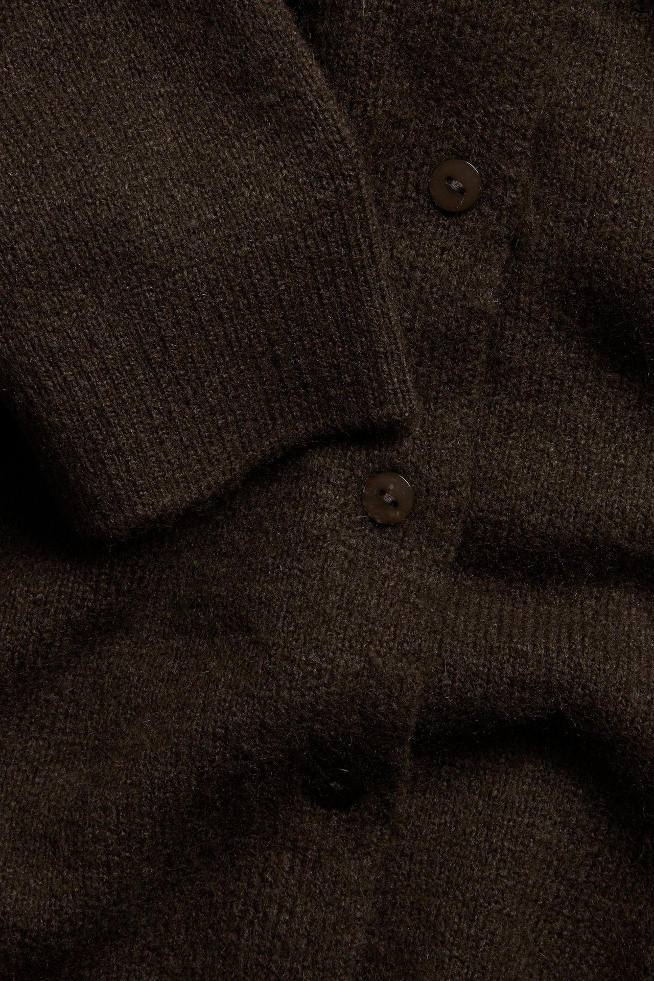 Nærbilde av en mørkebrun finstrikket cardigan med synlige knapper og ribbet mansjett.