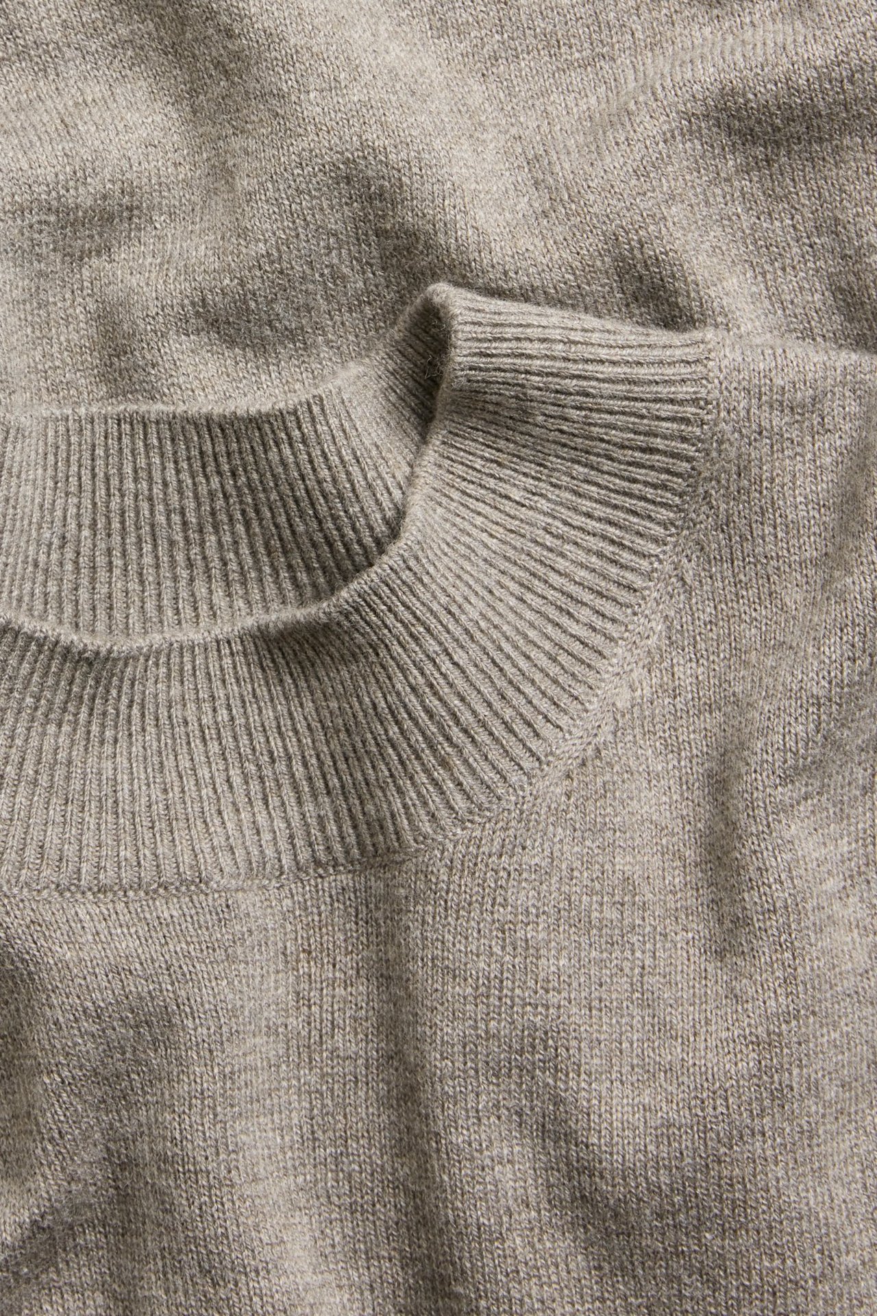 Zbliżenie na brązowy melanżowy, drobno dziergany sweter z golfem z mieszanki wełny, z prążkowanymi detalami.