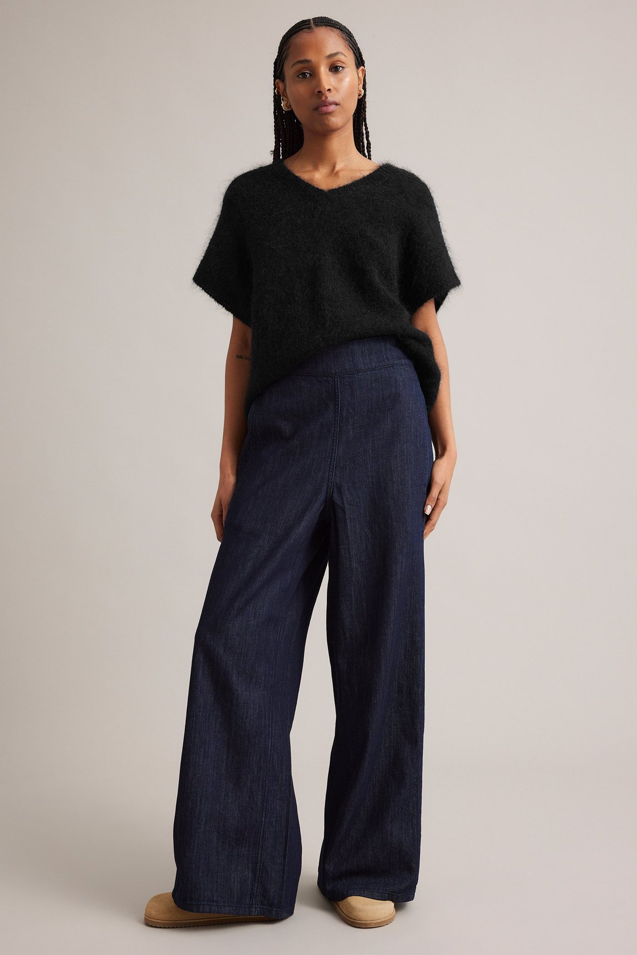 Framifrån: kvinna i svart fluffig mohairblandad V-ringad topp, mörkblå vida byxor och beiga skor.