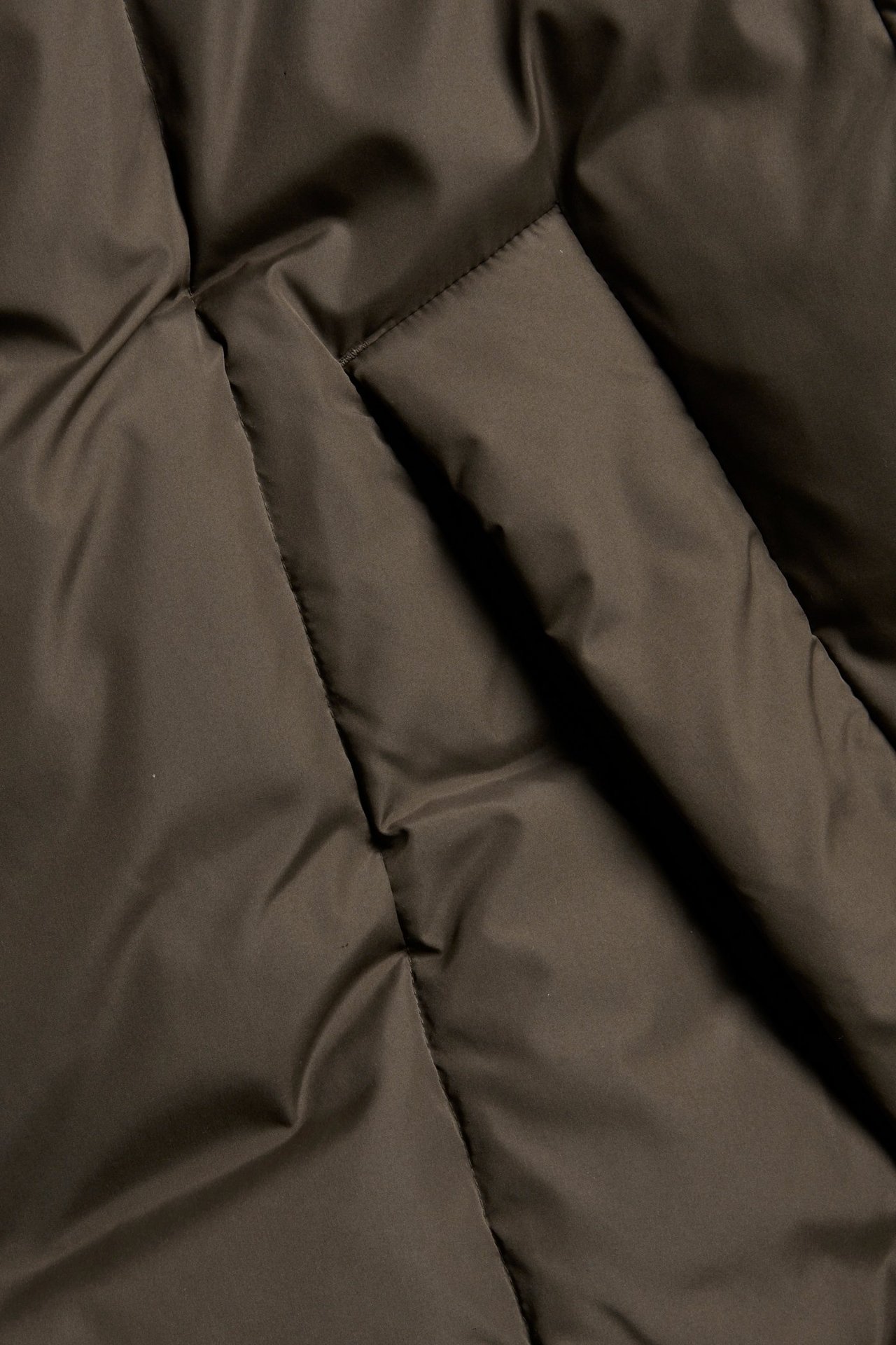 Zbliżenie brązowej pikowanej kurtki puchowej z widocznym detalem kieszeni.