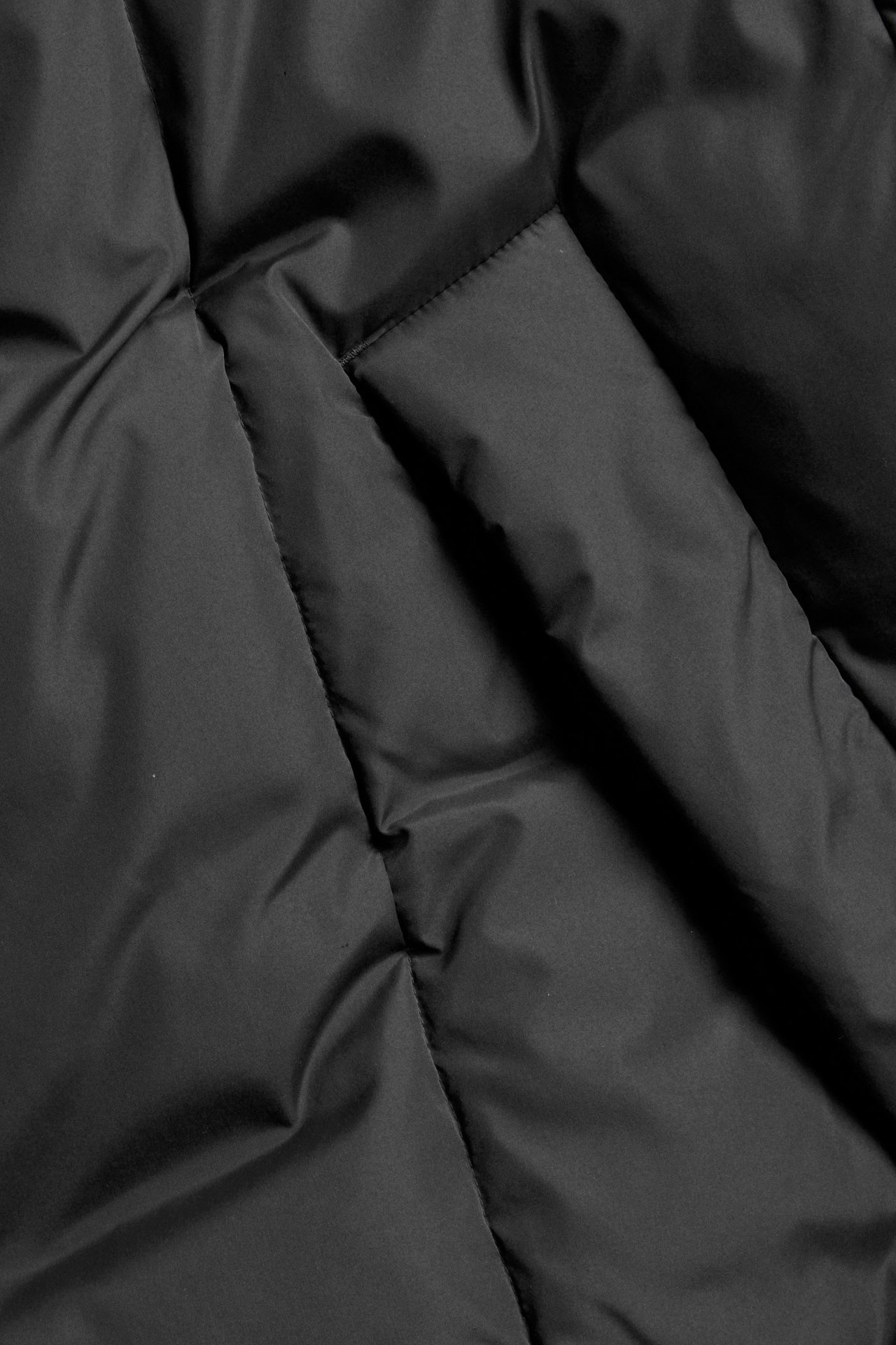 Zbliżenie na czarną, pikowaną kurtkę puchową z widoczną kieszenią.