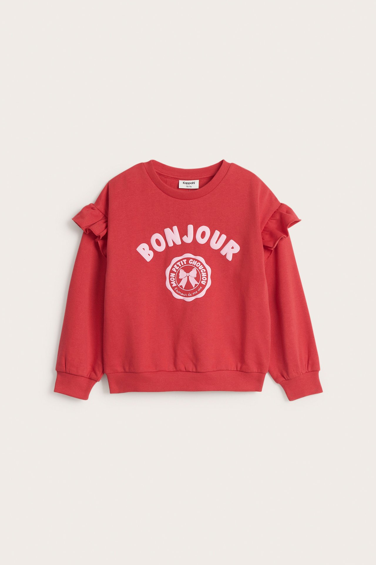 Frontvy av en röd barntröja med volanger på ärmarna och ett "BONJOUR"-tryck framtill.