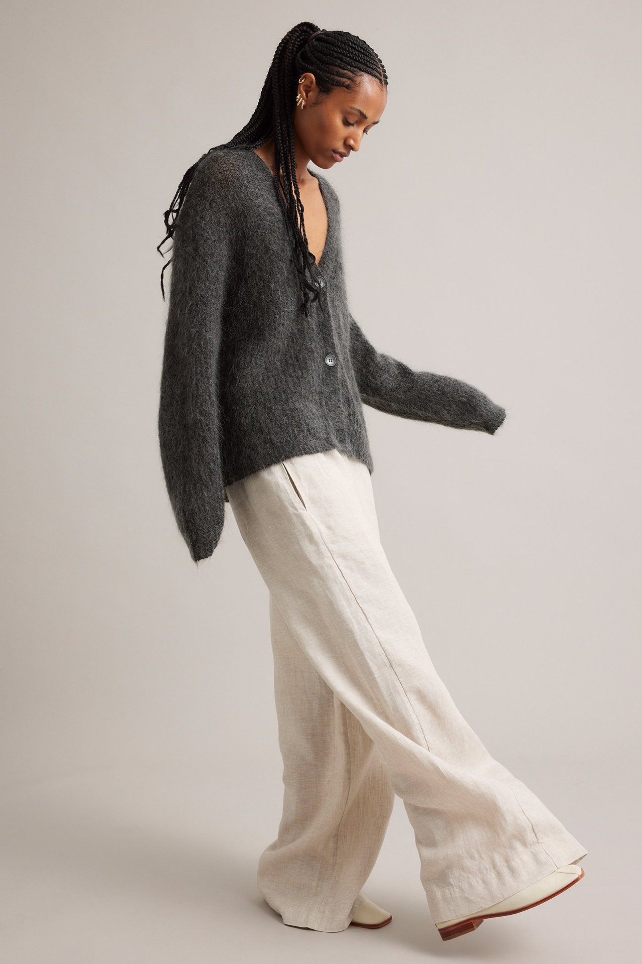 Framifrån: kvinna i mörkgrå mohairblandningskofta, ljusbeige vida byxor och krämfärgade skor.