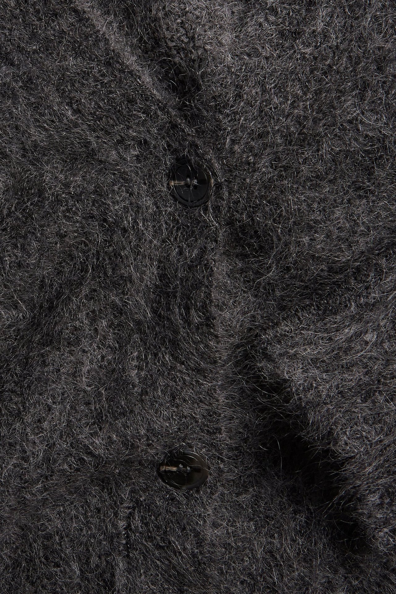 Zbliżenie szarego, puszystego kardiganu z mieszanki moheru z dwoma ciemnymi guzikami.
