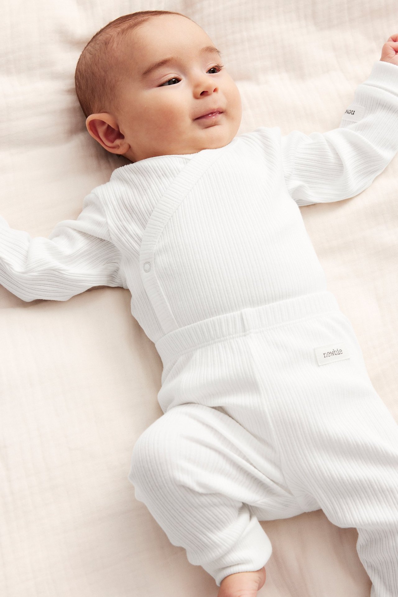 Ovenfra, baby i en offwhite ribbet omslagsbody med trykknapper og matchende ribbete bukser.