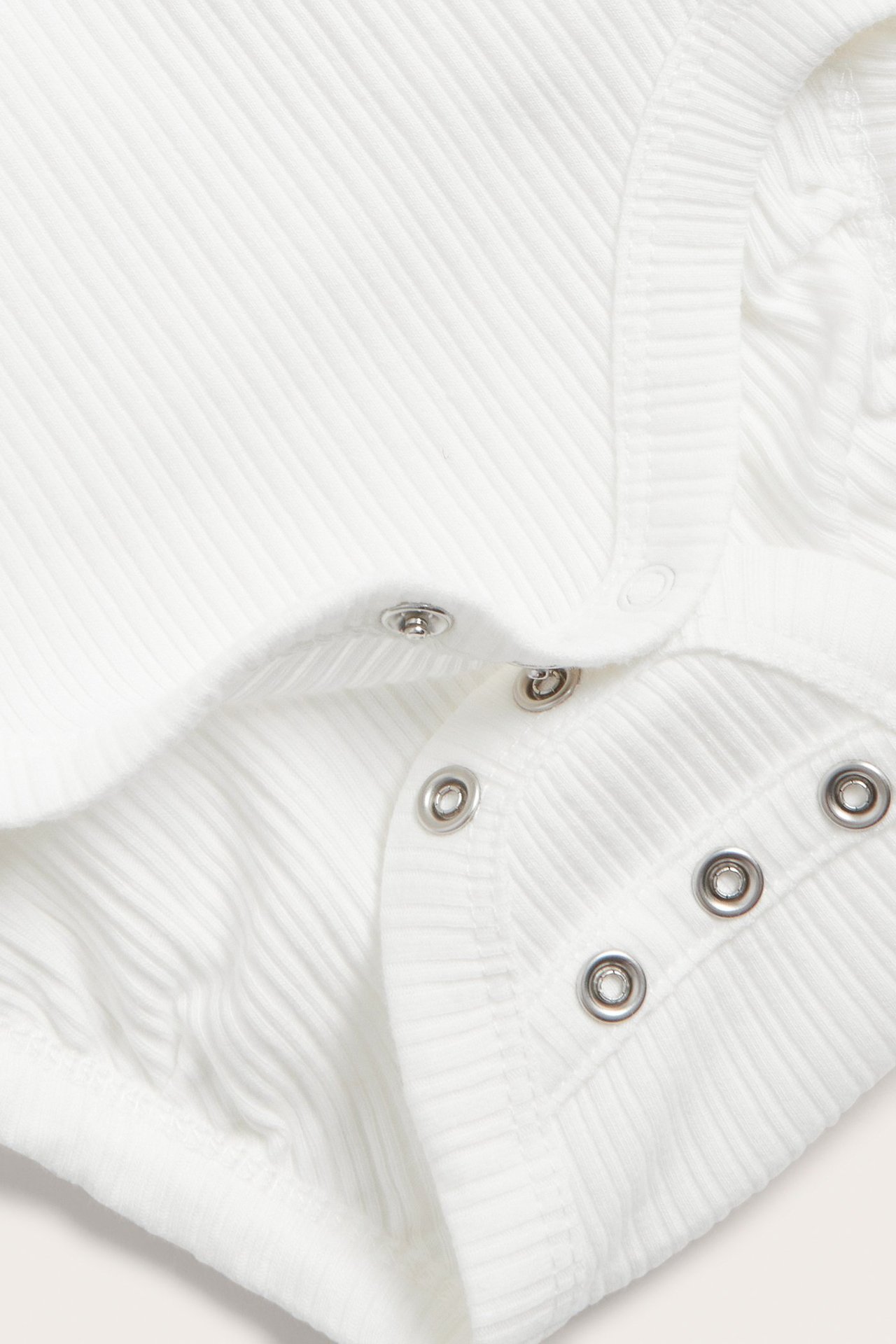 Zbliżenie na białe, prążkowane body kopertowe dla niemowląt ze srebrnymi zatrzaskami w kroku.