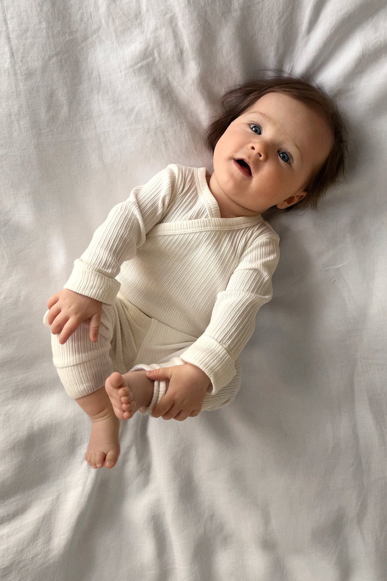 Widok z góry na dziecko w prążkowanym, kremowym body kopertowym z długimi rękawami i wywijanymi mankietami.