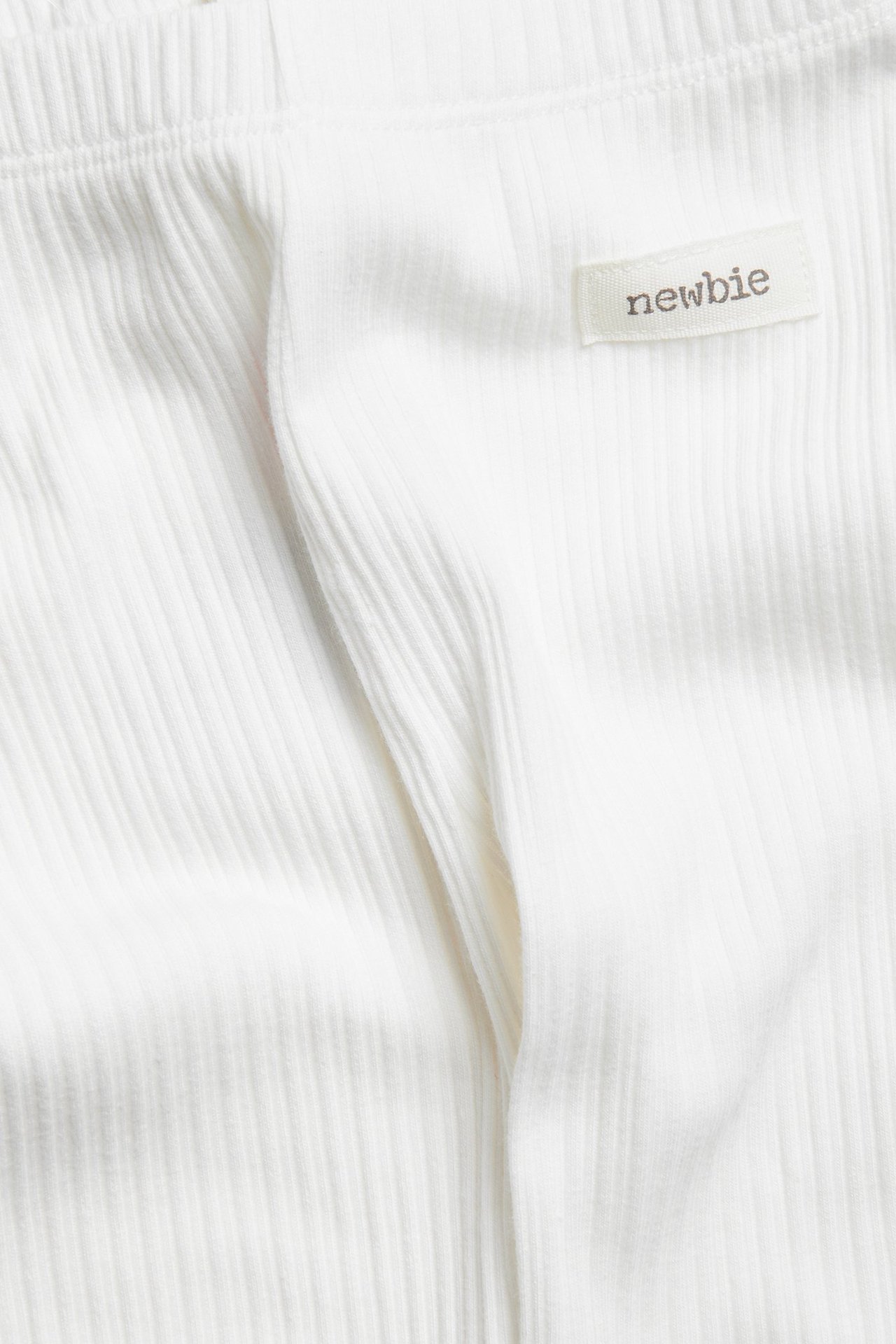 Zbliżenie na kremowobiałe prążkowane legginsy niemowlęce z metką "newbie".