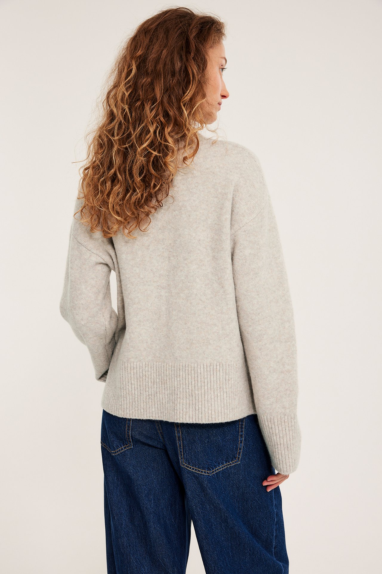 Klädd kvinna i ljusbeige stickad pullover med rundhals, melerad, långärmad, över blå jeans.