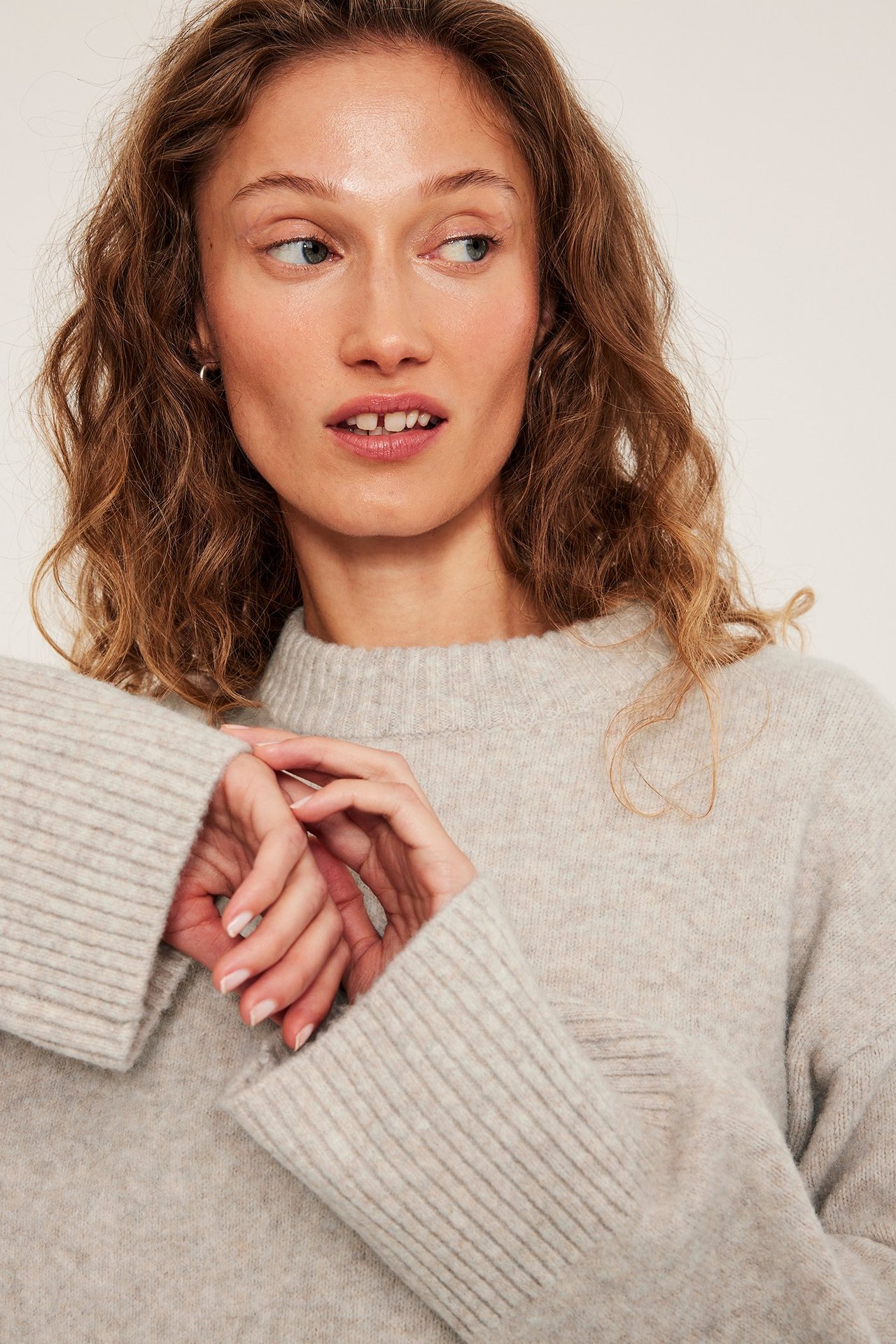 Kvinna med en ljusbeige stickad tröja med melerad pattern, rundhals, frontvy.