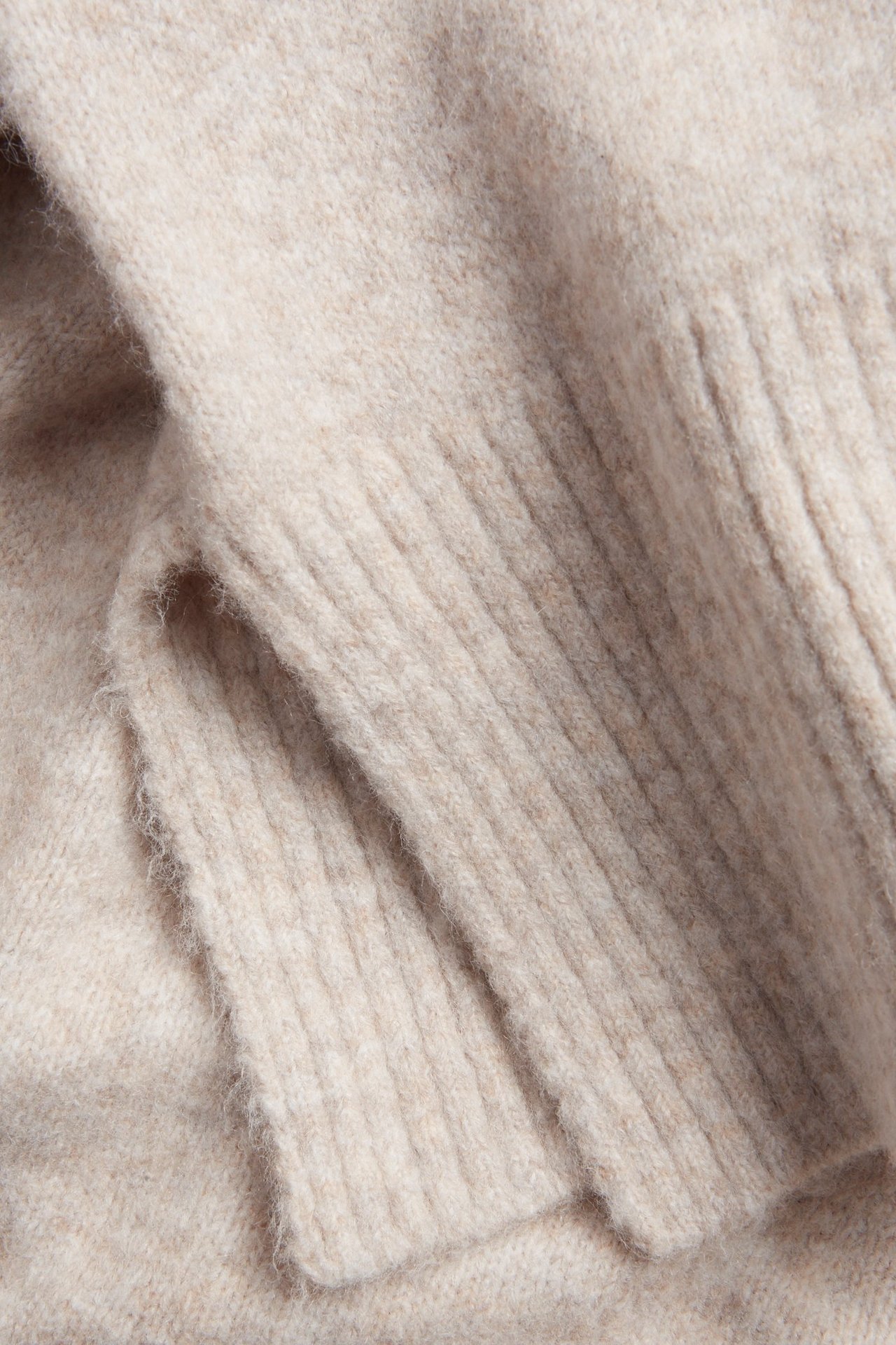 Zbliżenie jasnobeżowego melanżowego swetra dzianinowego z prążkowanymi detalami.