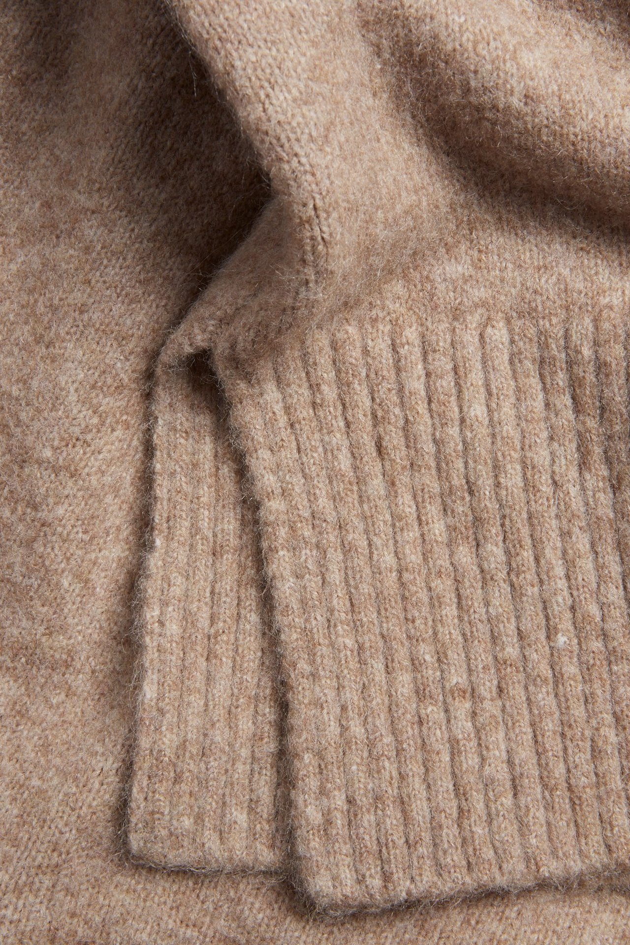 Zbliżenie na brązowy melanżowy sweter dzianinowy z jednolitym wzorem i prążkowanymi detalami.