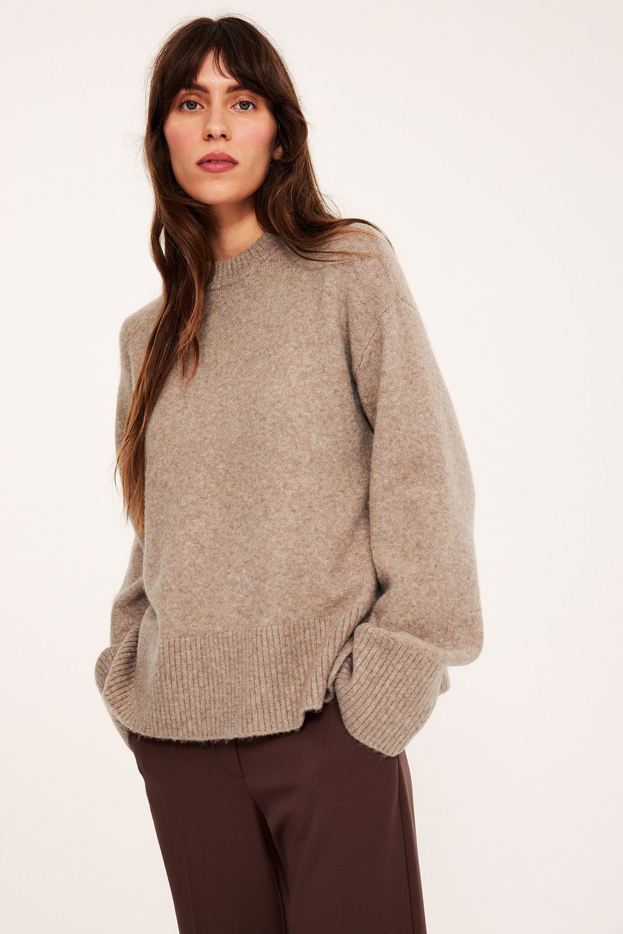 Edestäpäin: nainen yllään ruskeamelange neulottu pyöreäkauluksinen neule ja tummanruskeat housut.