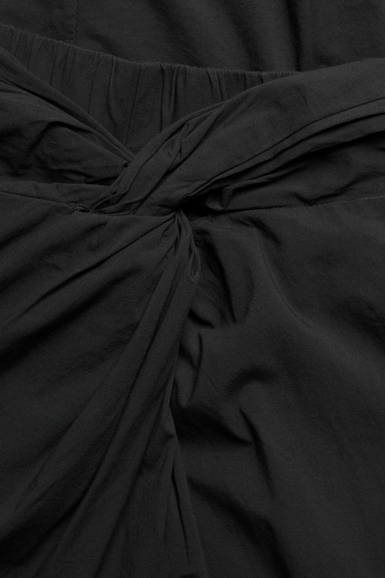 Zbliżenie czarnej spódnicy midi z mieszanki bawełny i wiskozy z węzłem z przodu.