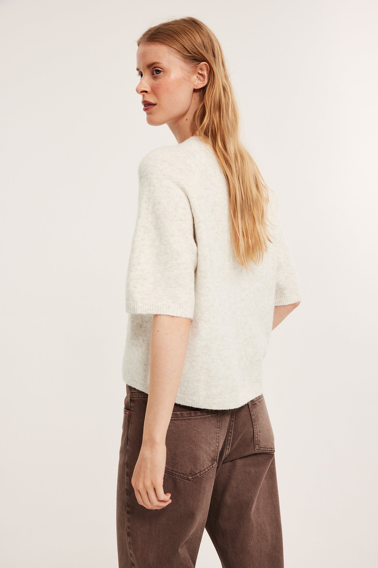 Sidovy av en kvinna i en oversized ljusbeige melerad stickad t-shirt och bruna byxor.