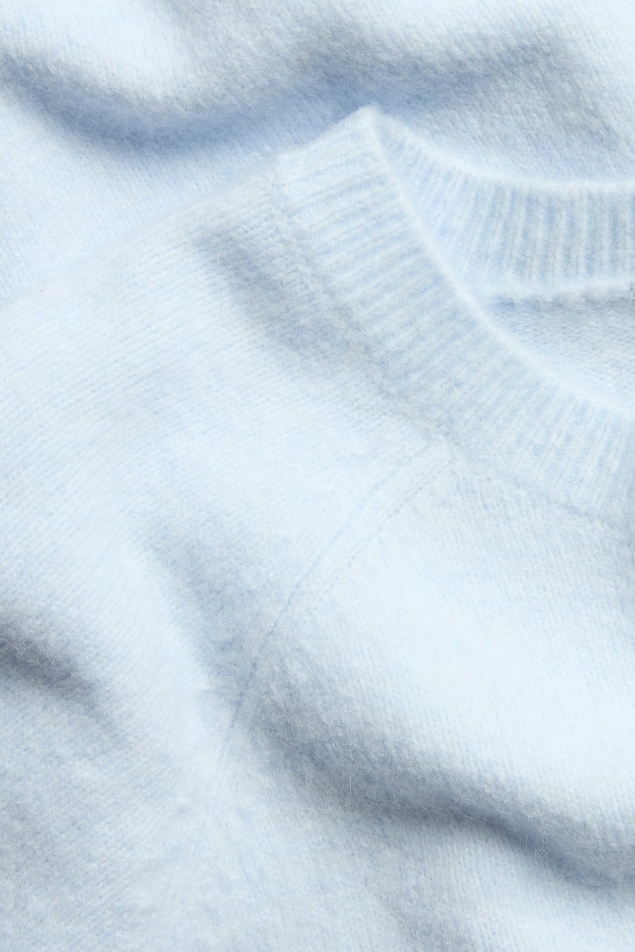 Lähikuva vaaleansinisestä, ylisuuresta neulotusta t-paidasta pyöreällä kaula-aukolla ja yksivärisellä kuviolla.