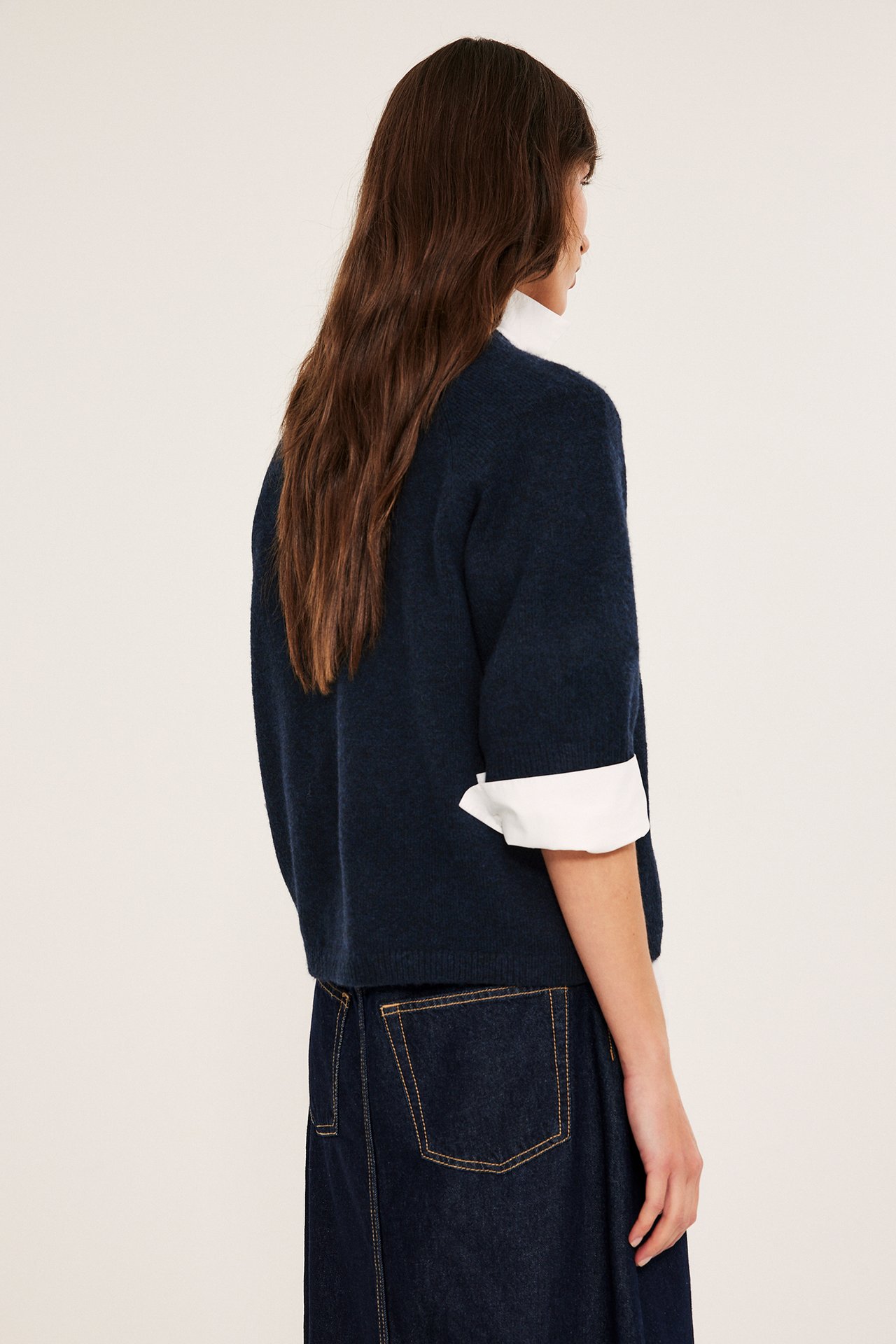 Kvinna från sidan i en mörkblå oversized stickad t-shirt över vit skjorta, med jeanskjol.