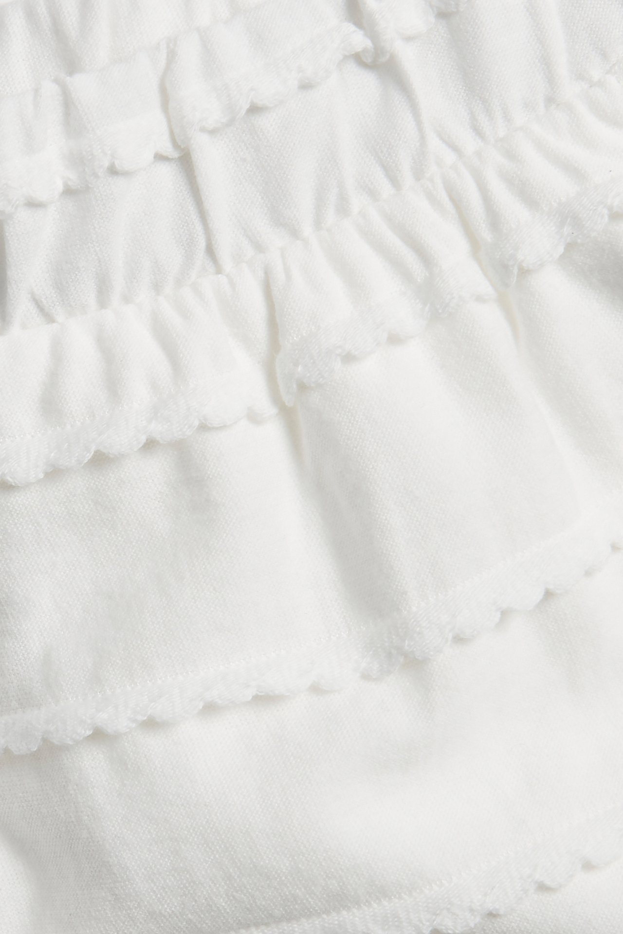 Nærbilde av offwhite pyjamasshorts i bomull med dekorative volanglag.