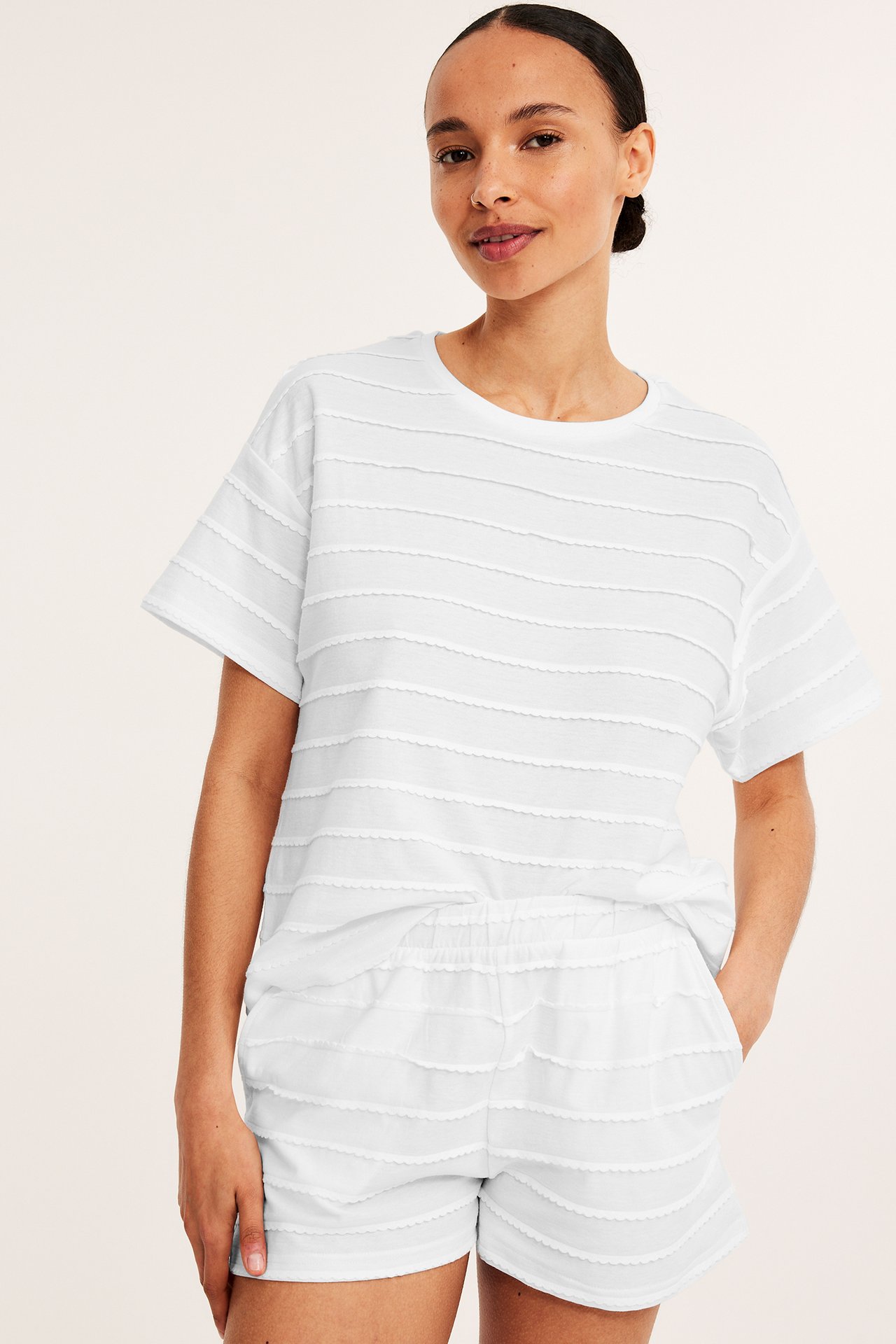 Frontbilde av en kvinne i offwhite pyjamasshorts med strukturstriper og matchende kortermet topp.