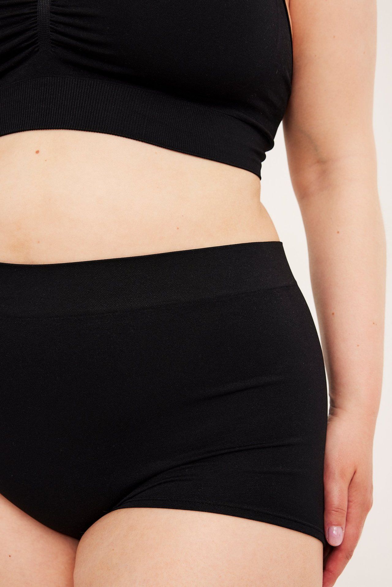 Närbild av en kvinna i svarta sömlösa boxertrosor och en svart behåtopp.