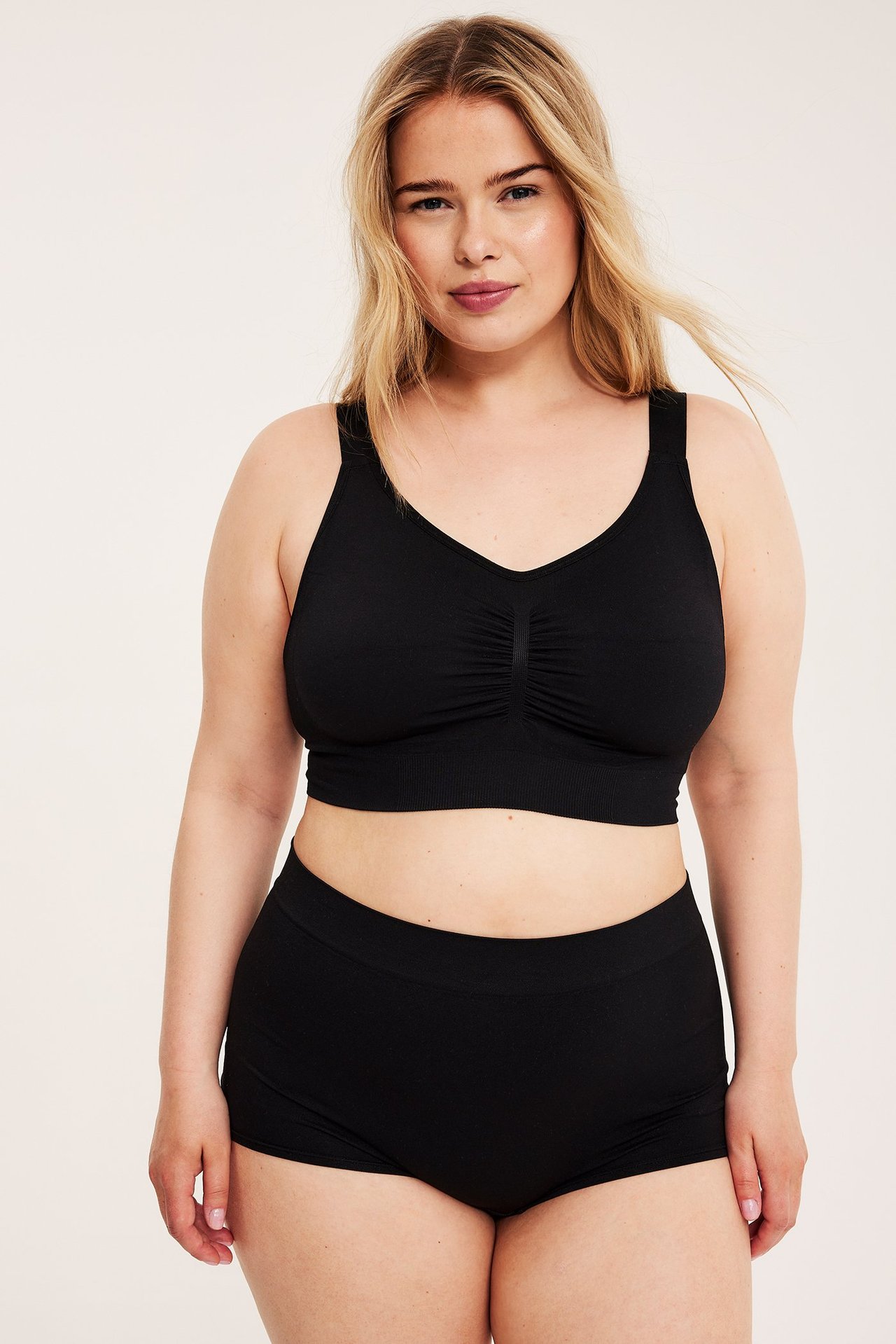Forfra, kvinne i svarte sømløse boksershorts og matchende svart sømløs BH.