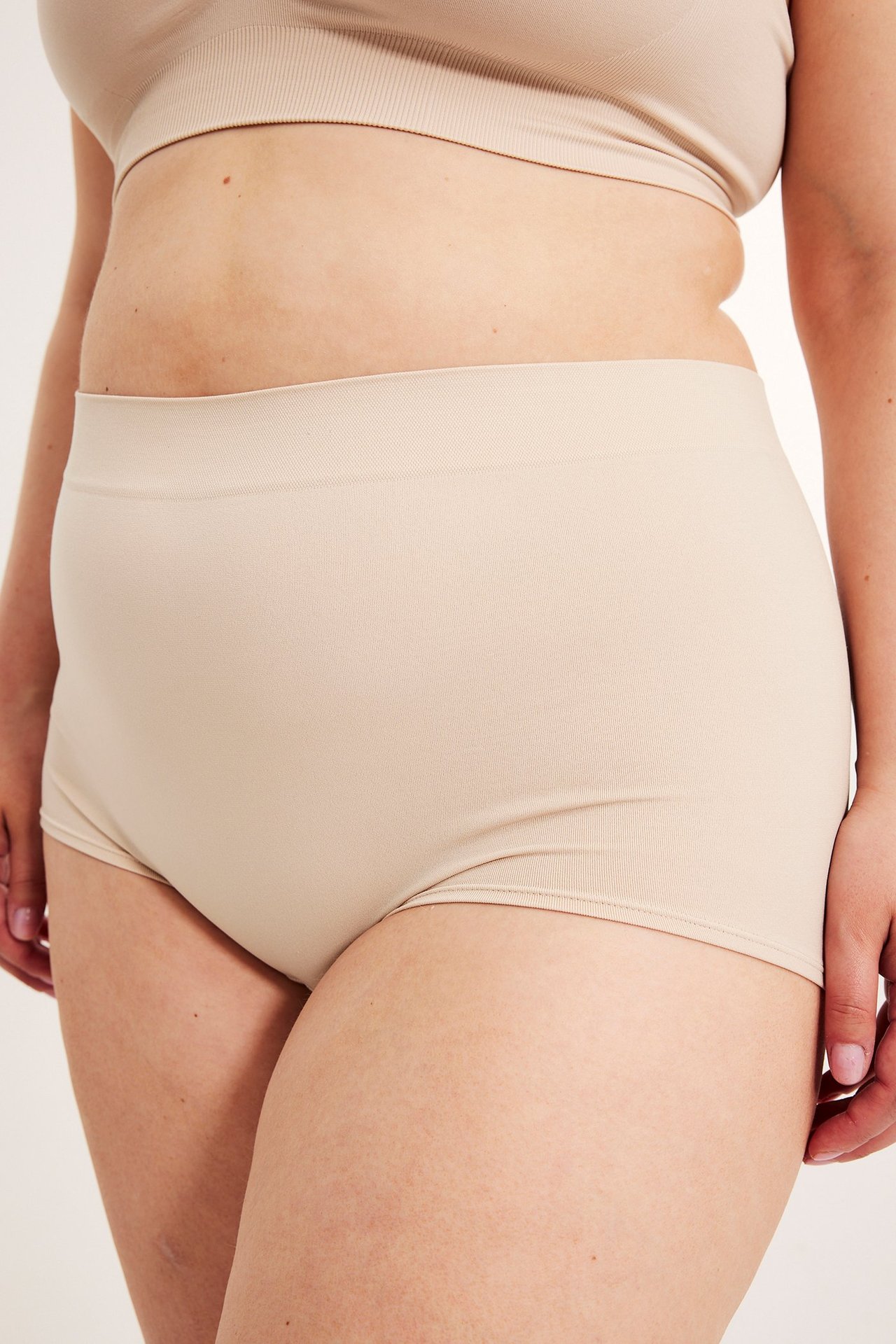 Sidovy av kvinna i ljusrosa sömlösa högmidjade boxertrosor och matchande BH-topp.