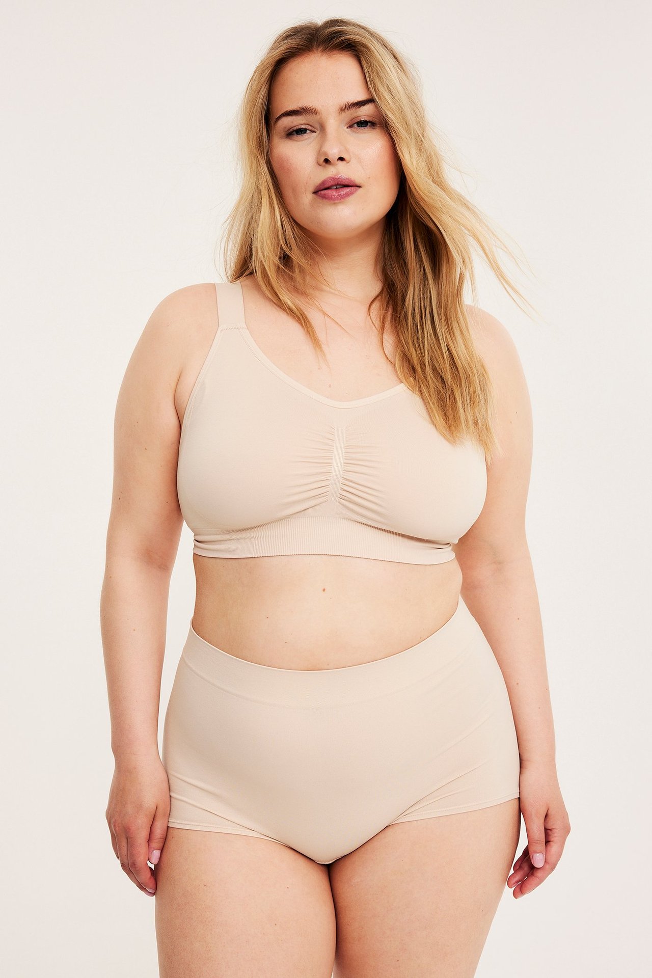 Forfra: kvinne i lys rosa sømløs boxershorts og matchende sømløs BH.