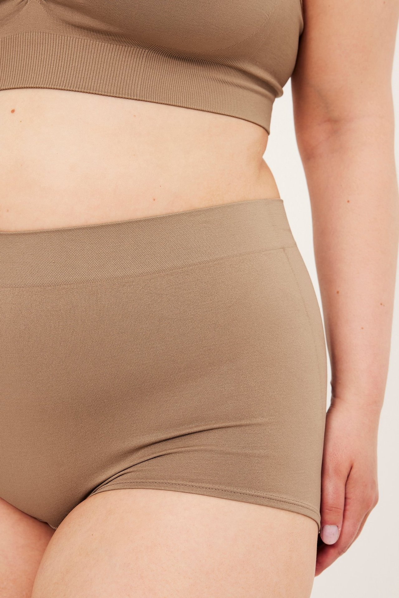 Nærbilde, sidevisning av en kvinne i beige sømløse boksershorts og matchende BH-topp.