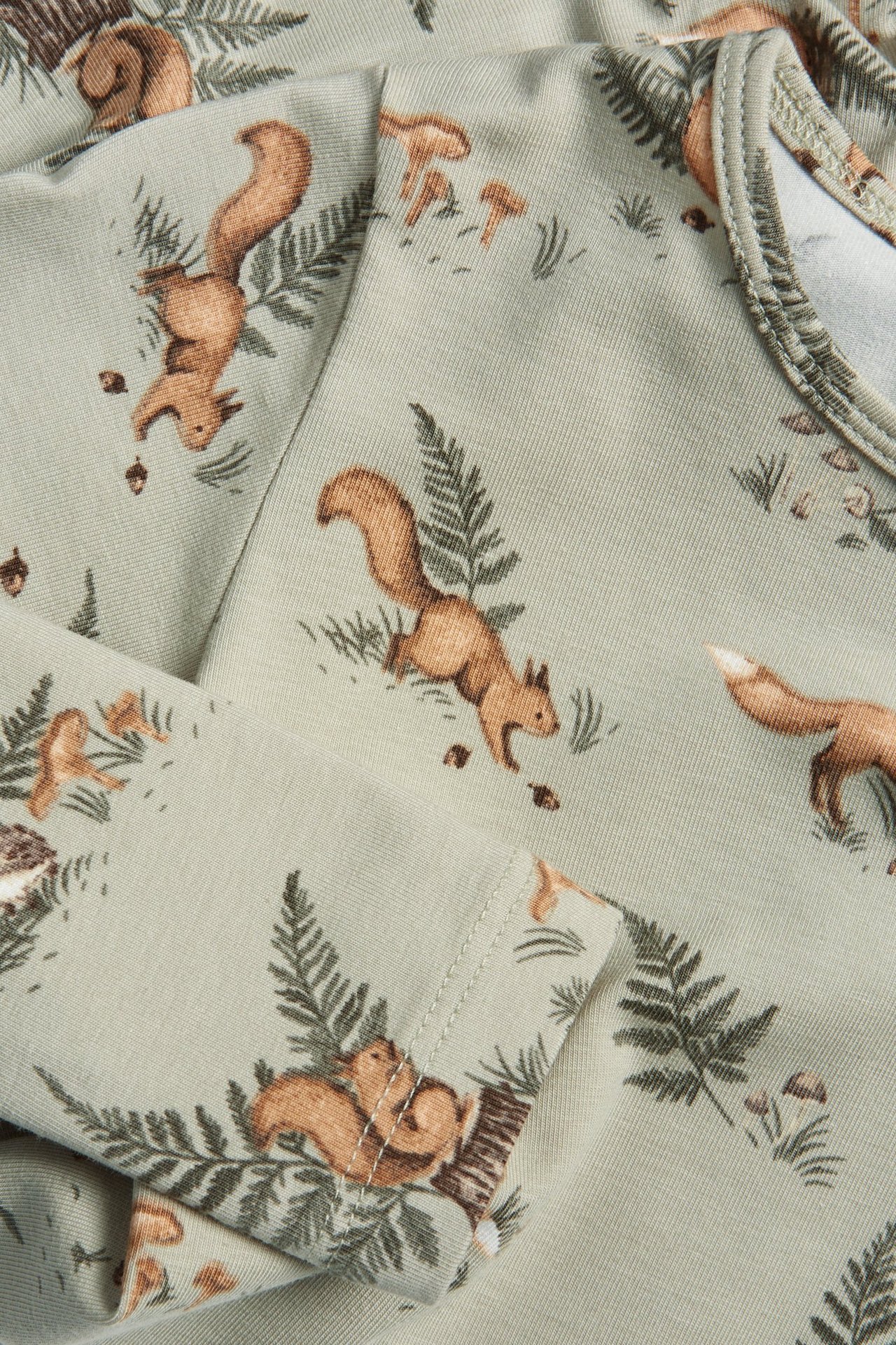 Lähikuva vaaleanvihreästä pitkähihaisesta vauvan puuvillabodysta, jossa on orava- ja metsäkuvio.