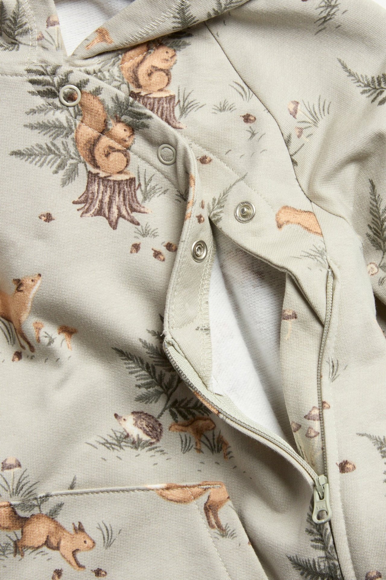 Nærbilde av lys grønn babyoverall med skogsdyrmønster, glidelås og trykknapper foran.