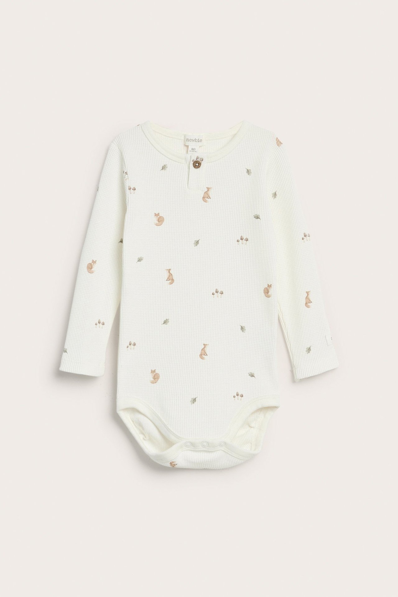Frontvisning av en offwhite vaffelstrikket babybody med lange ermer, dyremønster og halsknapper.
