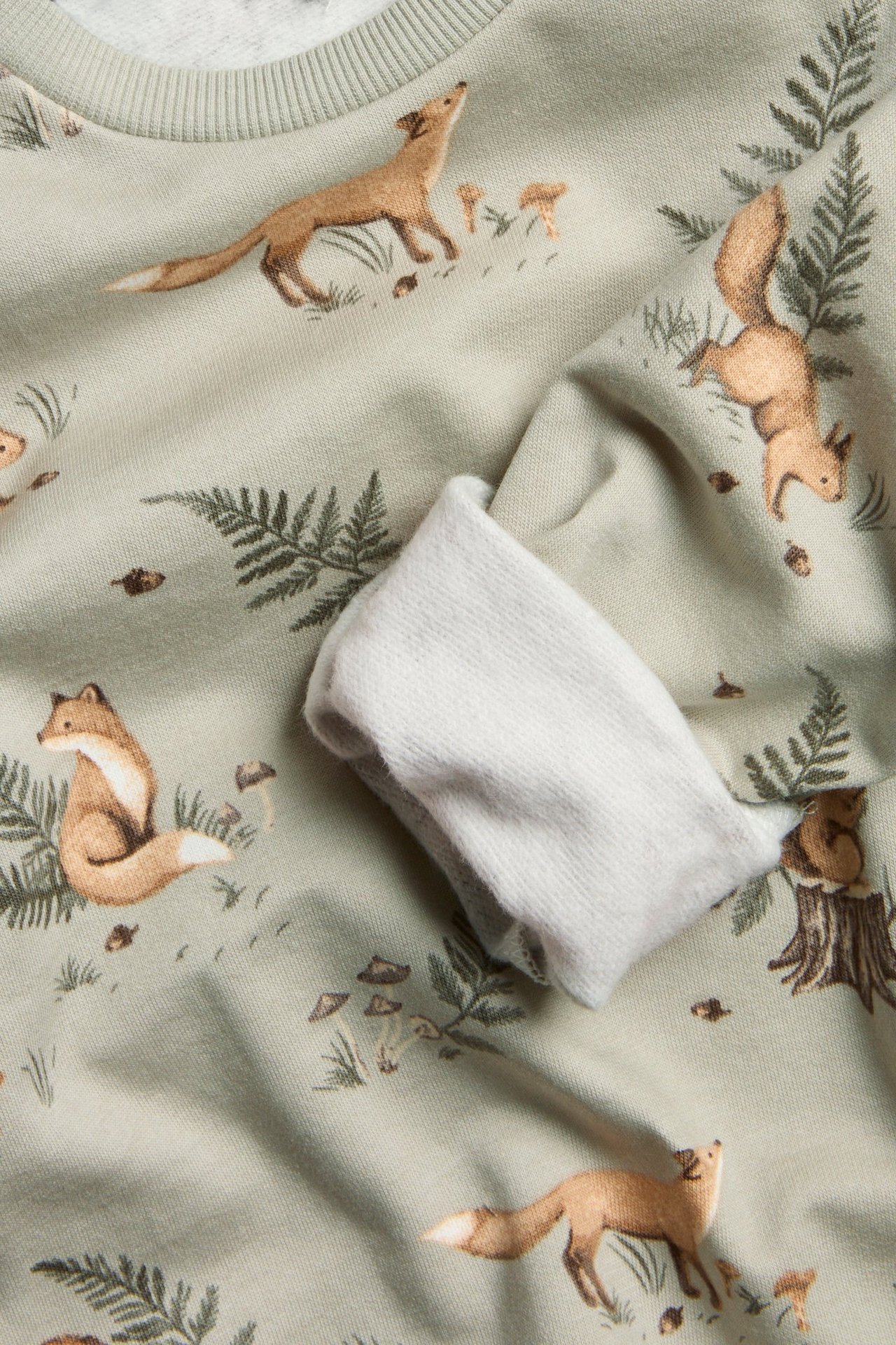 Zbliżenie na jasnozieloną bawełnianą bluzę dziecięcą z leśnym wzorem i prążkowanymi mankietami.