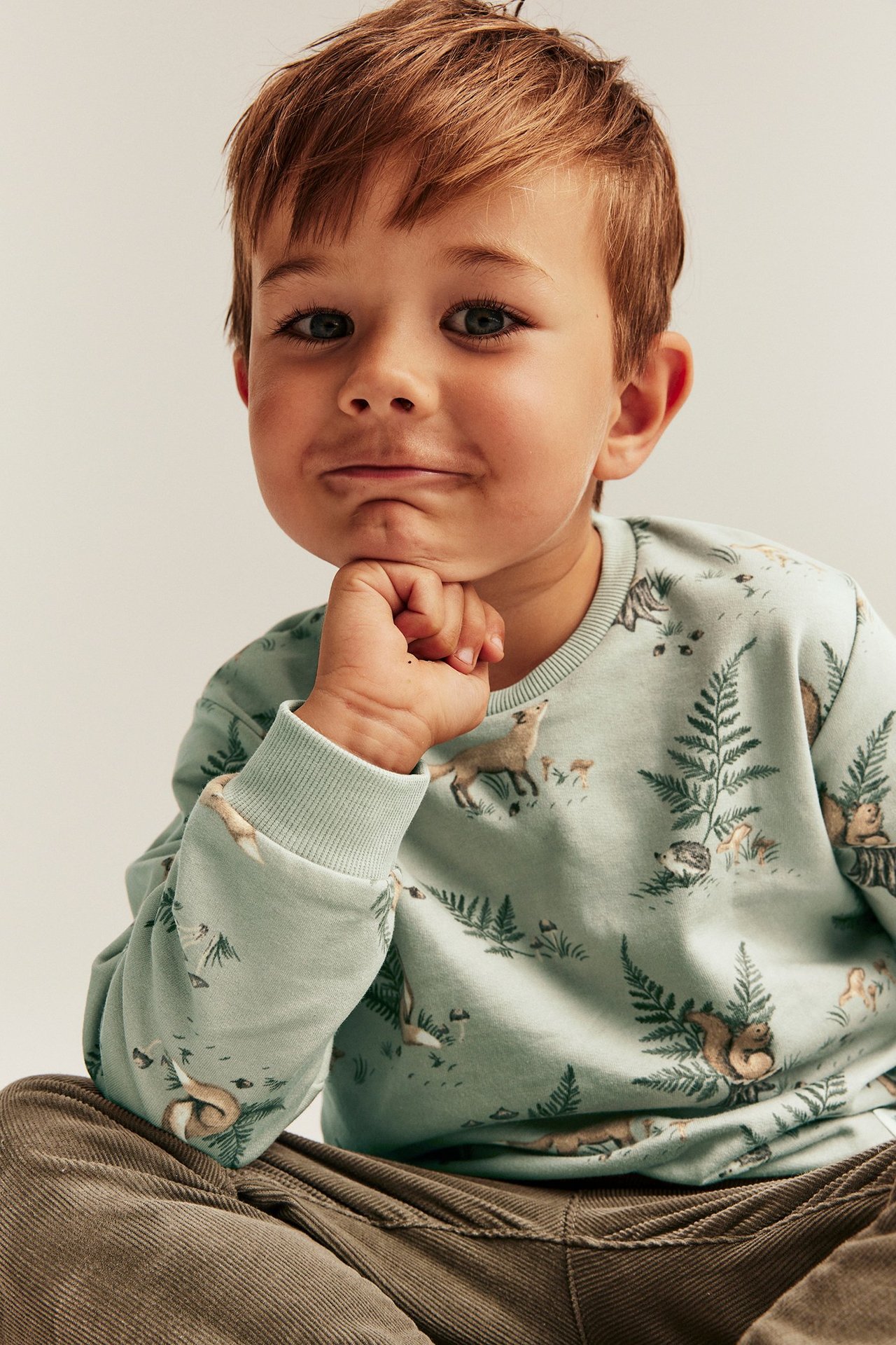 Lähikuva lapsesta vaaleanvihreässä puuvillapaidassa, jossa on metsäneläinkuvio ja ruskeat vakosamettihousut.