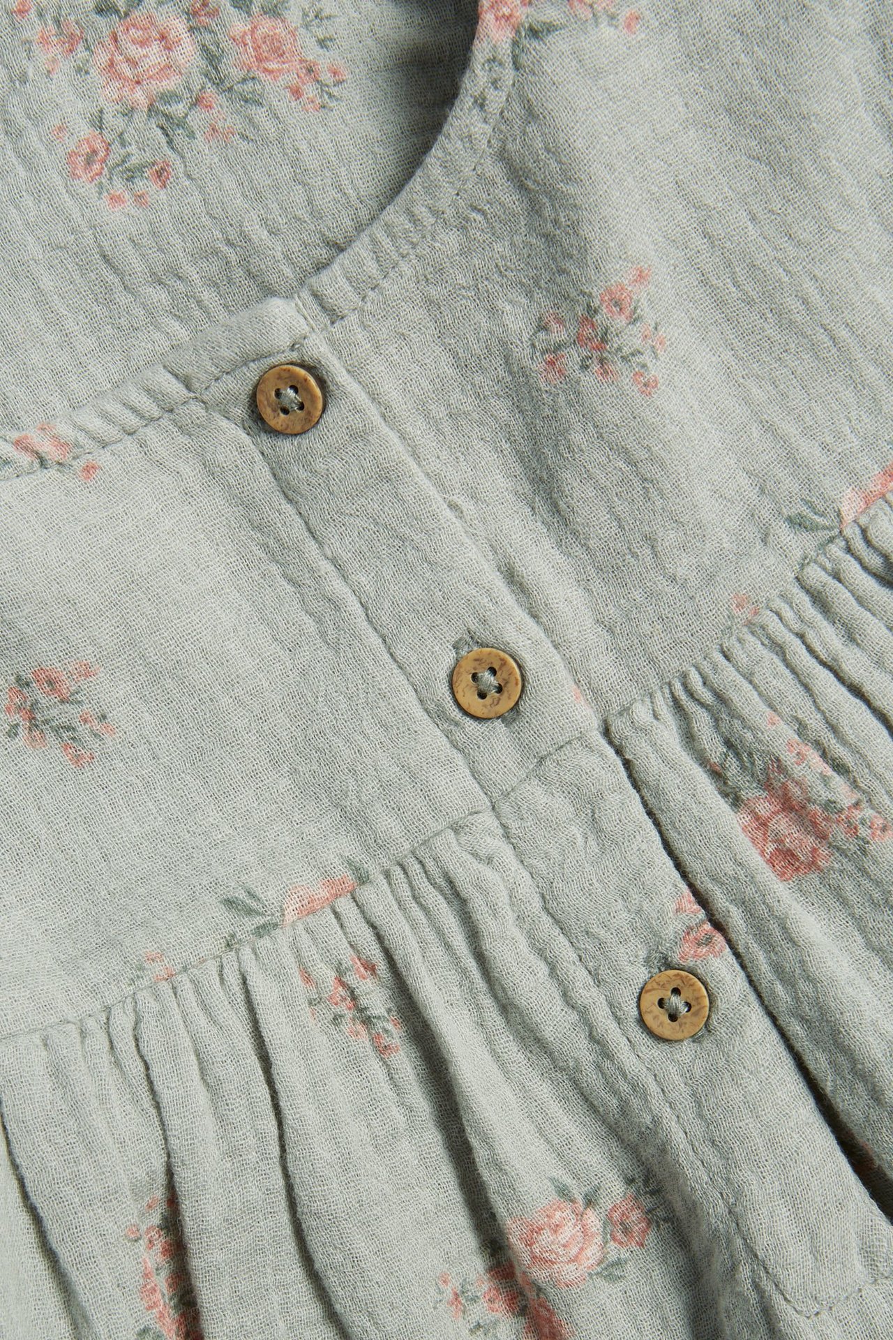 Zbliżenie na jasnozieloną tkaną bawełnianą sukienkę w drobne różowe kwiaty z drewnianymi guzikami.