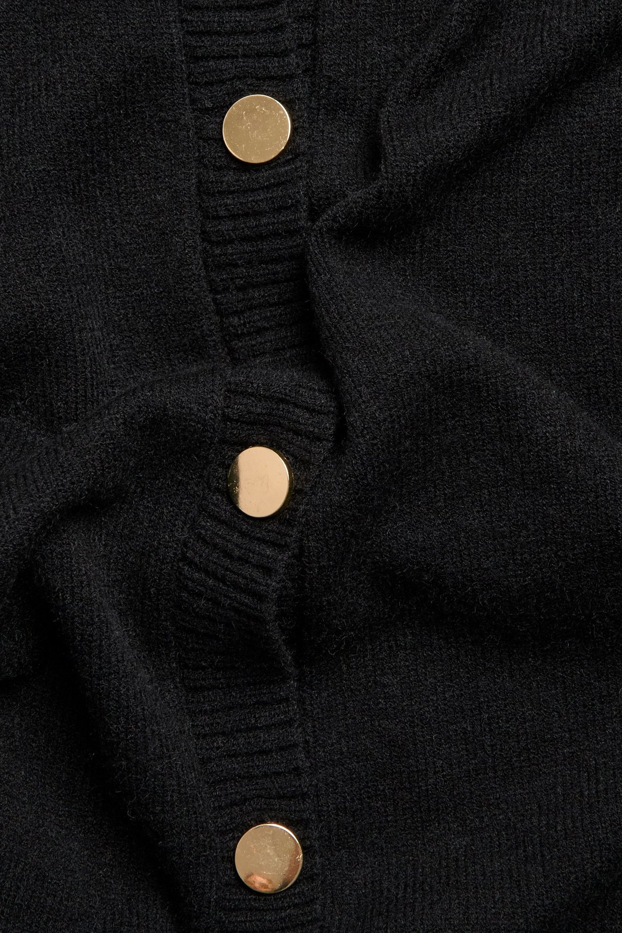 Zbliżenie czarnej dzianinowej kamizelki z trzema złotymi guzikami.
