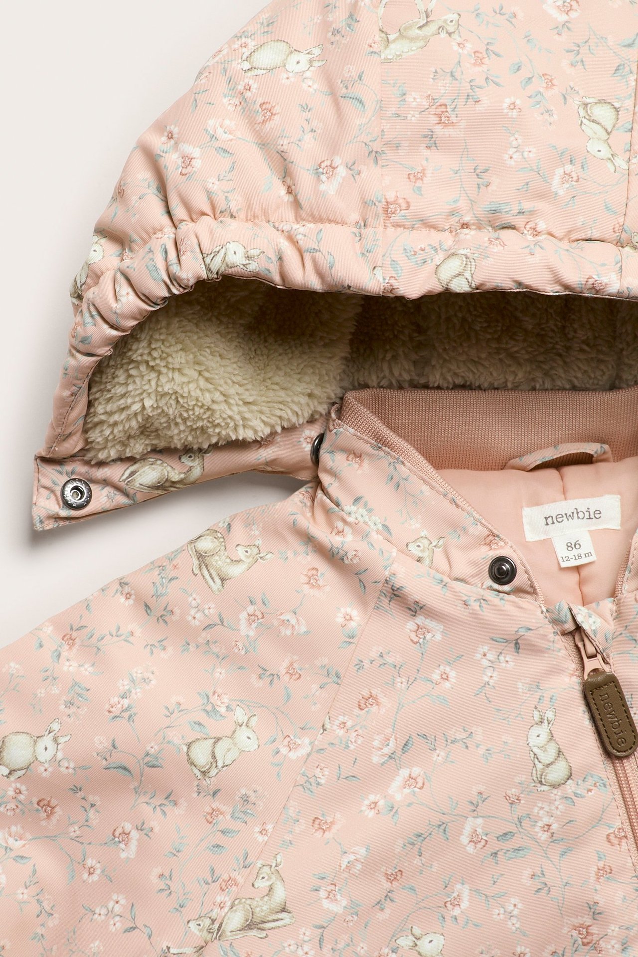 Zbliżenie: Różowy ocieplany kombinezon niemowlęcy w kwiaty i zwierzęta, z kapturem na misiu, zamek z przodu.