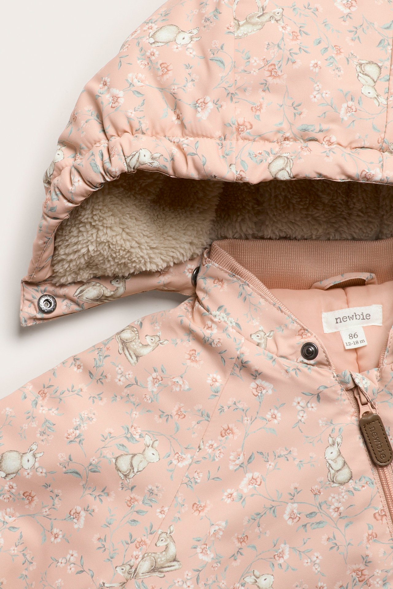 Zbliżenie na różowy kombinezon niemowlęcy z kwiatowo-zwierzęcym wzorem, puszystym kapturem i zamkiem.