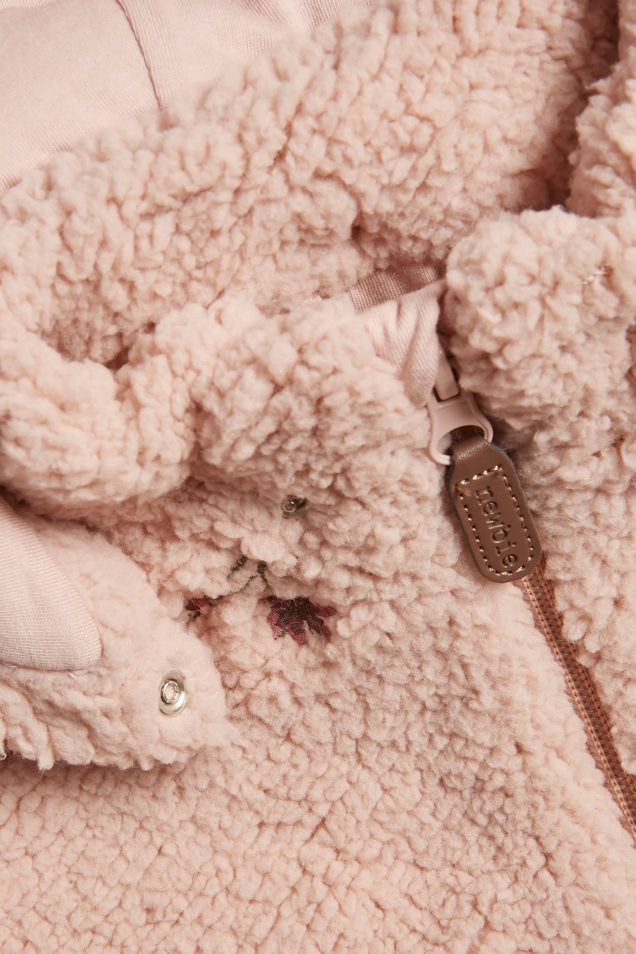 Nærbilde av en rosa barne-pilejakke med blomsterbroderi, glidelås og trykknapp.