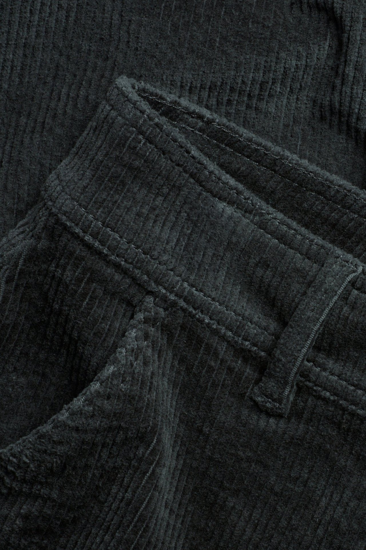 Zbliżenie szarych sztruksowych spodni, pokazujące pas, szlufki i otwór kieszeni.