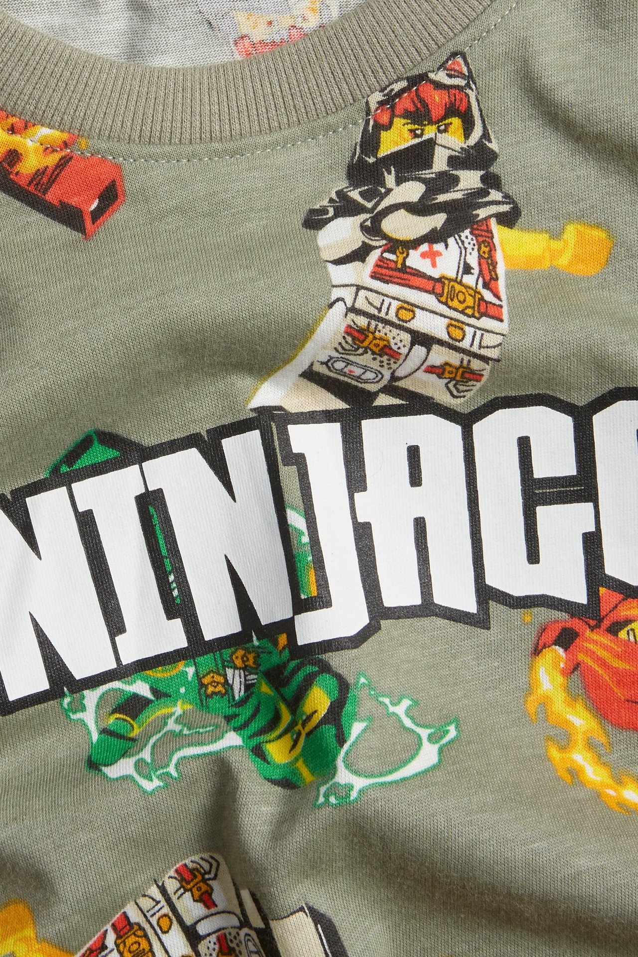 Närbild på mörkgrön oversized bomulls-t-shirt för barn med färgglatt Ninjago allover-tryck och ribbad hals.